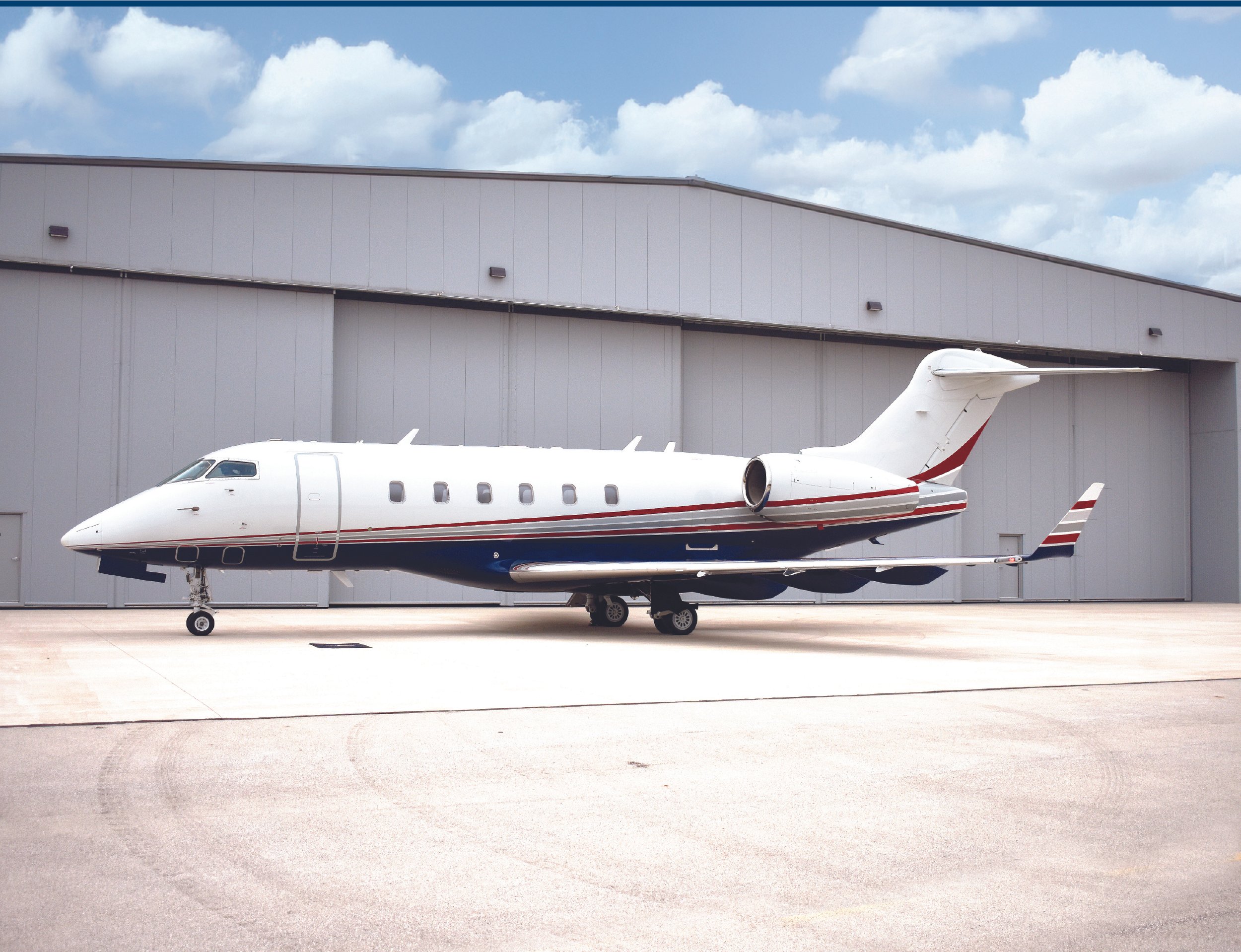 Small private jet parked outside a large hangar under a partly cloudy sky.