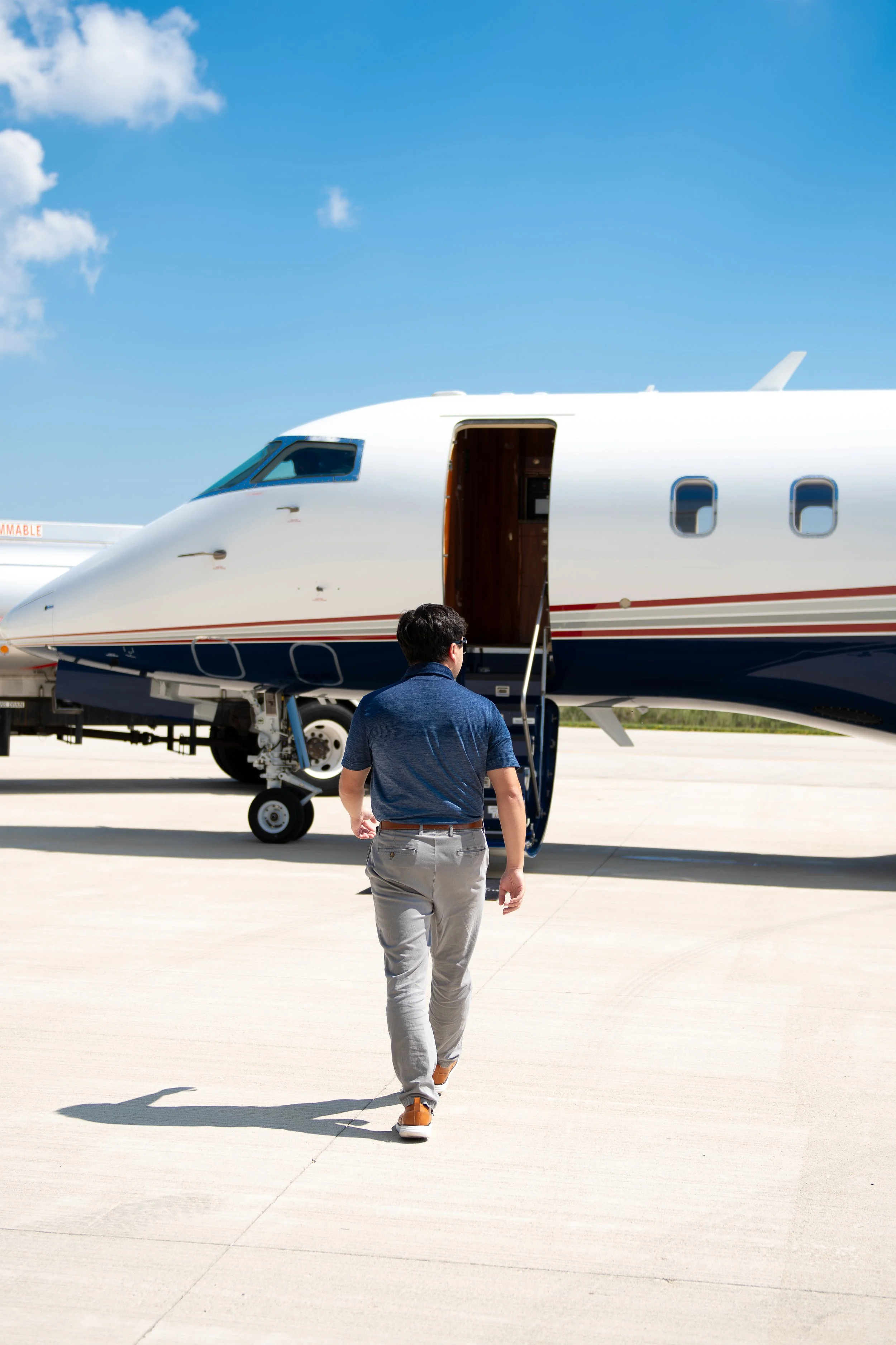A man walking toward a private jet on an airport tarmac under a blue sky with a few clouds.