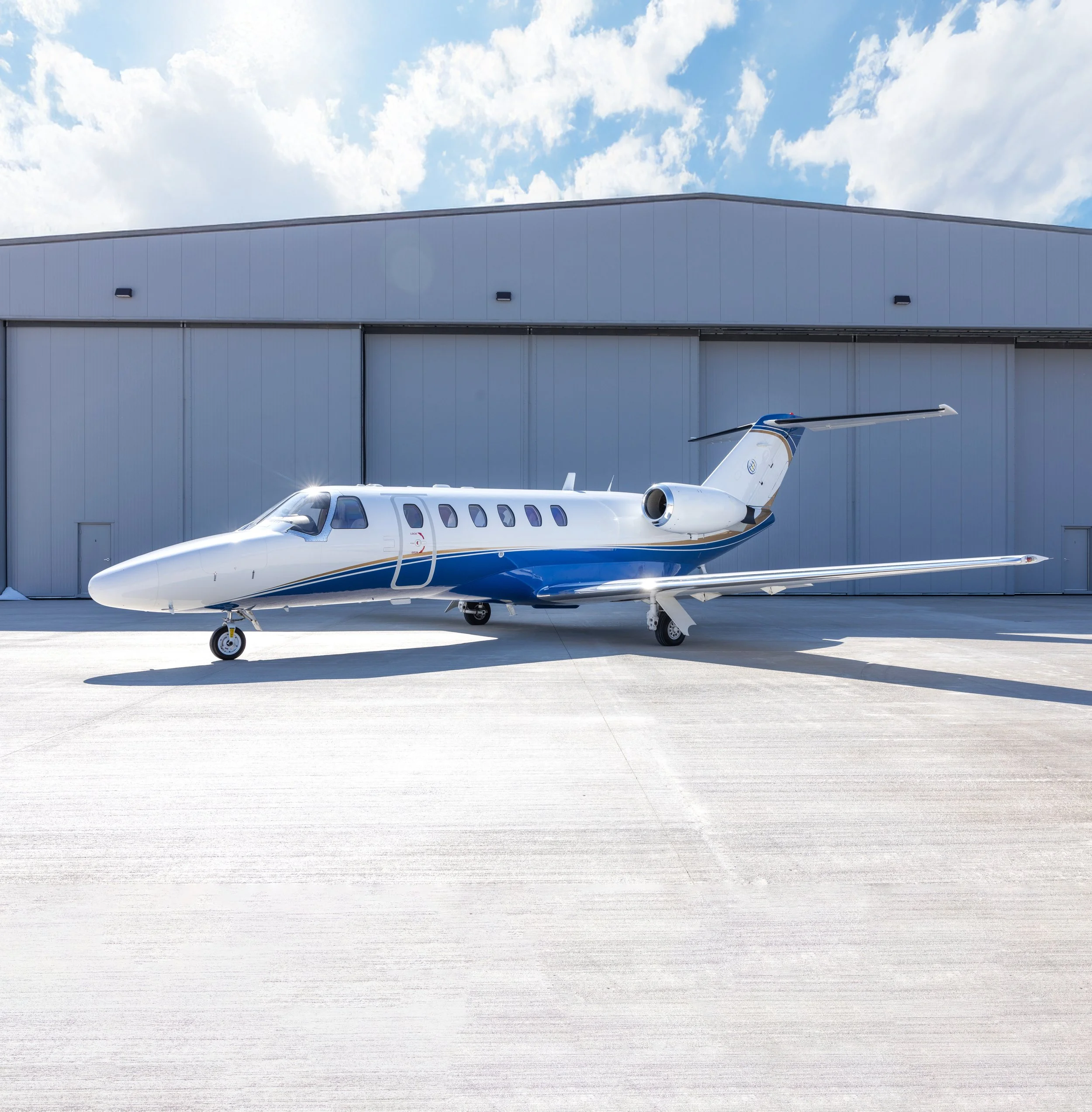 Private jet airplane parked outside hangar on tarmac on sunny day.