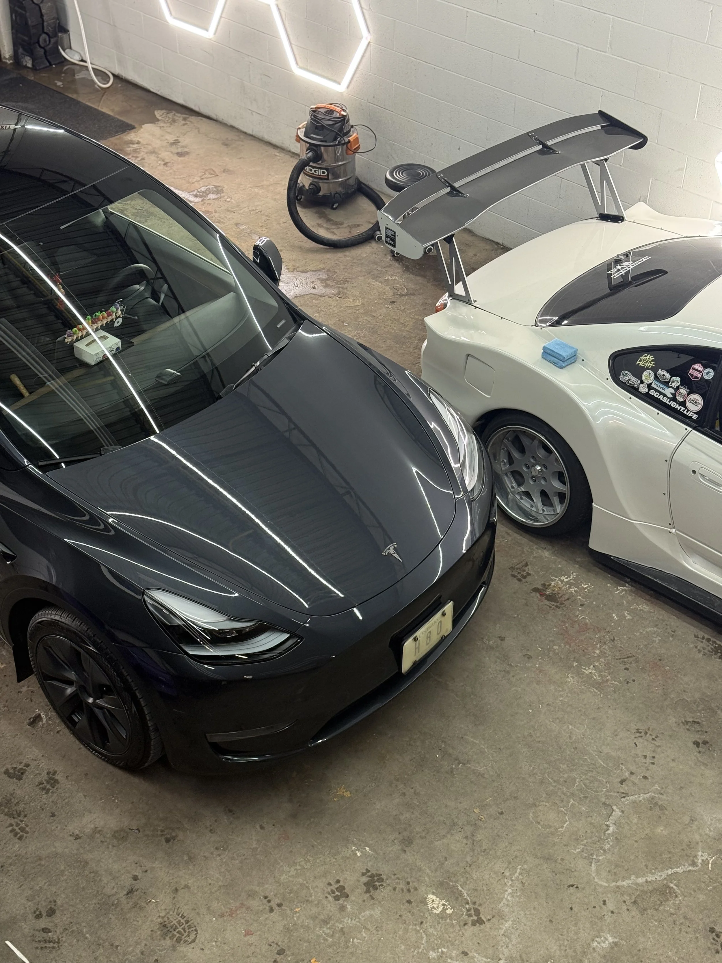 Black Tesla beside a white modified coupe inside the detailing studio