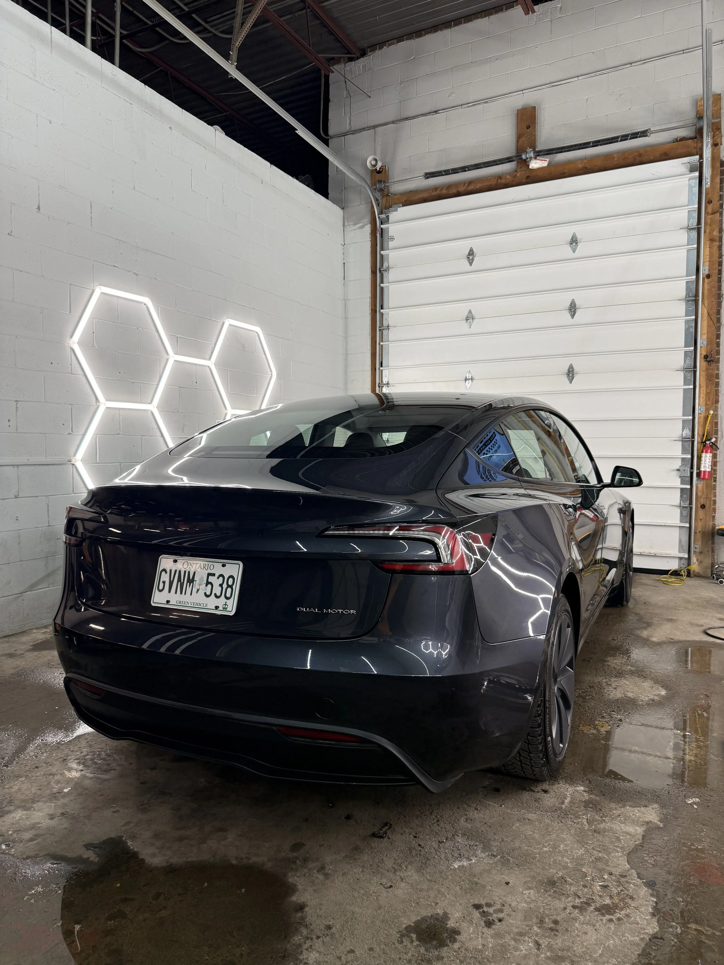 Black Tesla sedan under hex lights inside the detailing studio