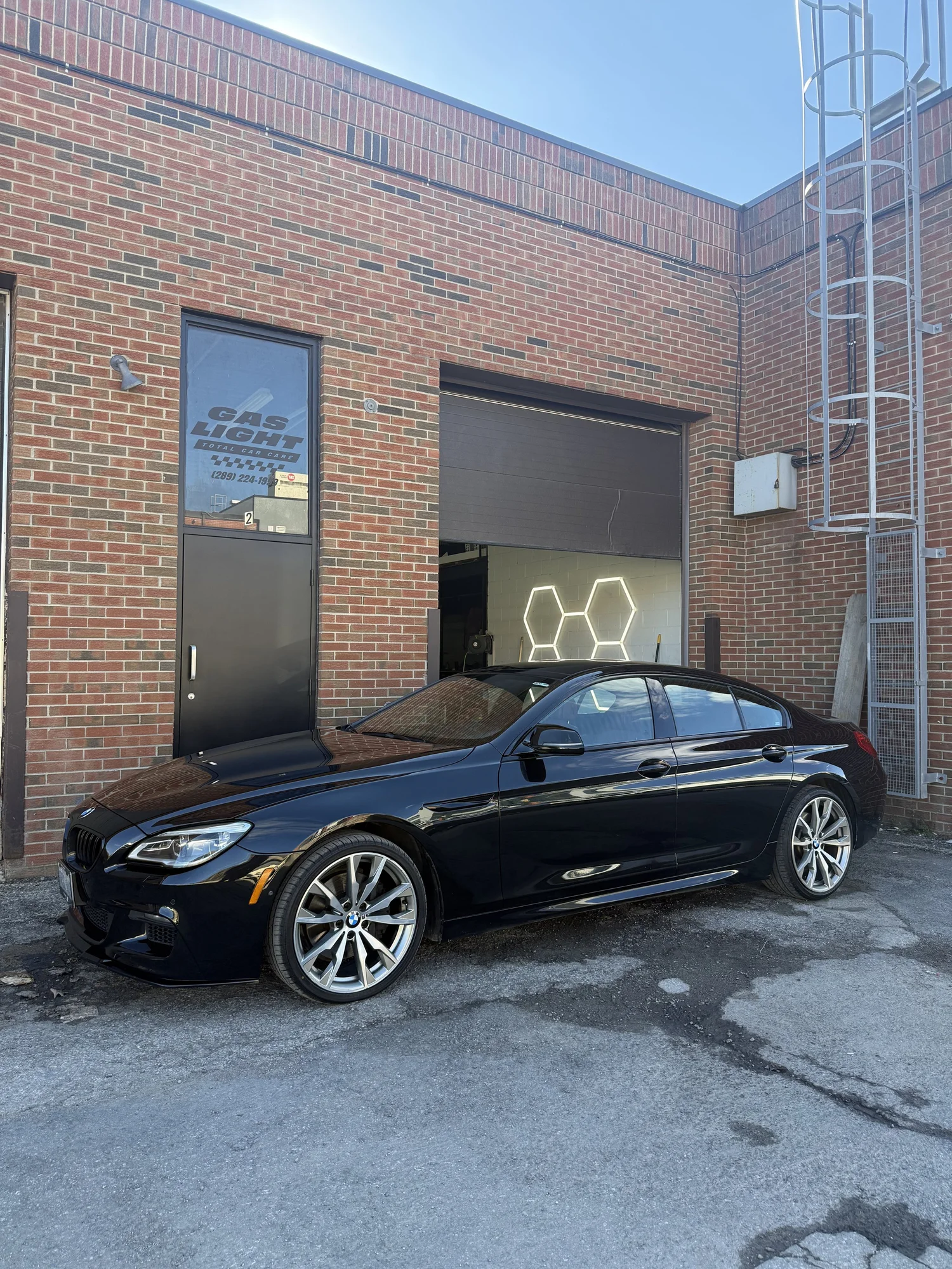 Glossy black BMW sedan outside Ultraviolet Detailing Studio in Maple