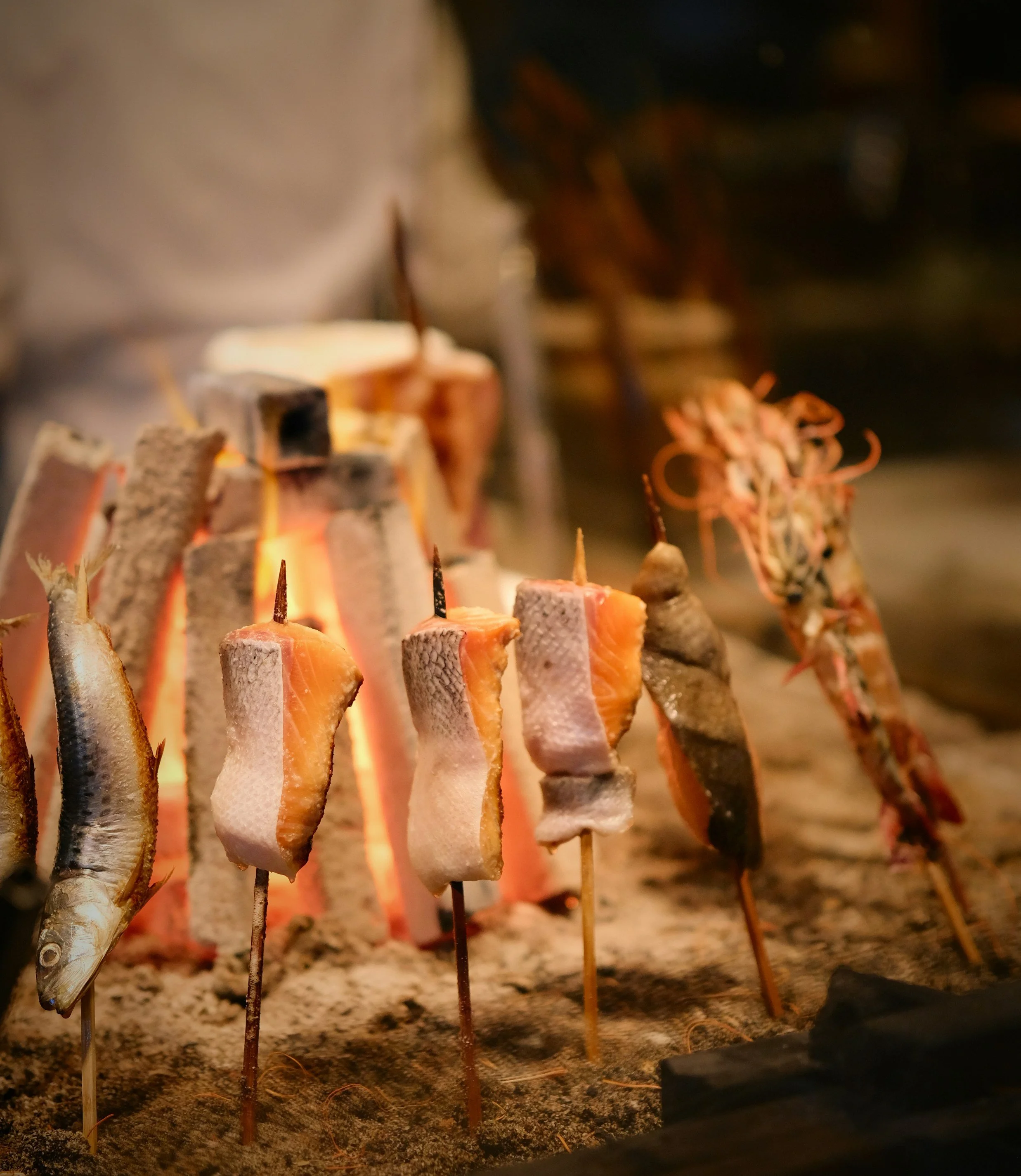 Close-up of skewers with grilled fish pieces over an open flame.