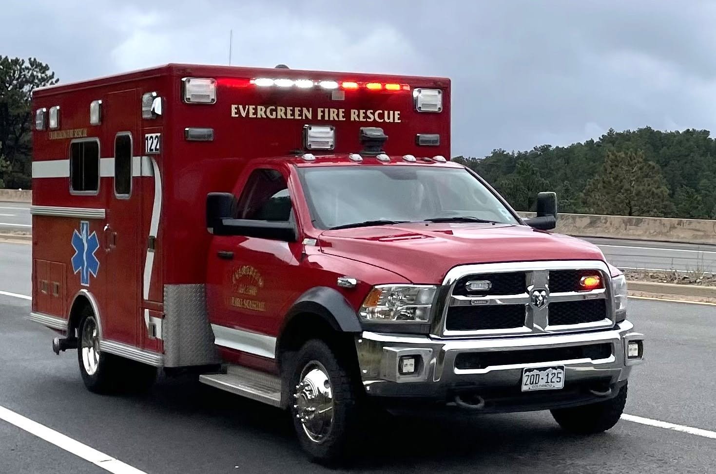 Red emergency rescue vehicle on the road with the words "Evergreen Fire Rescue" on it, a blue star of life symbol, and emergency lights on top.