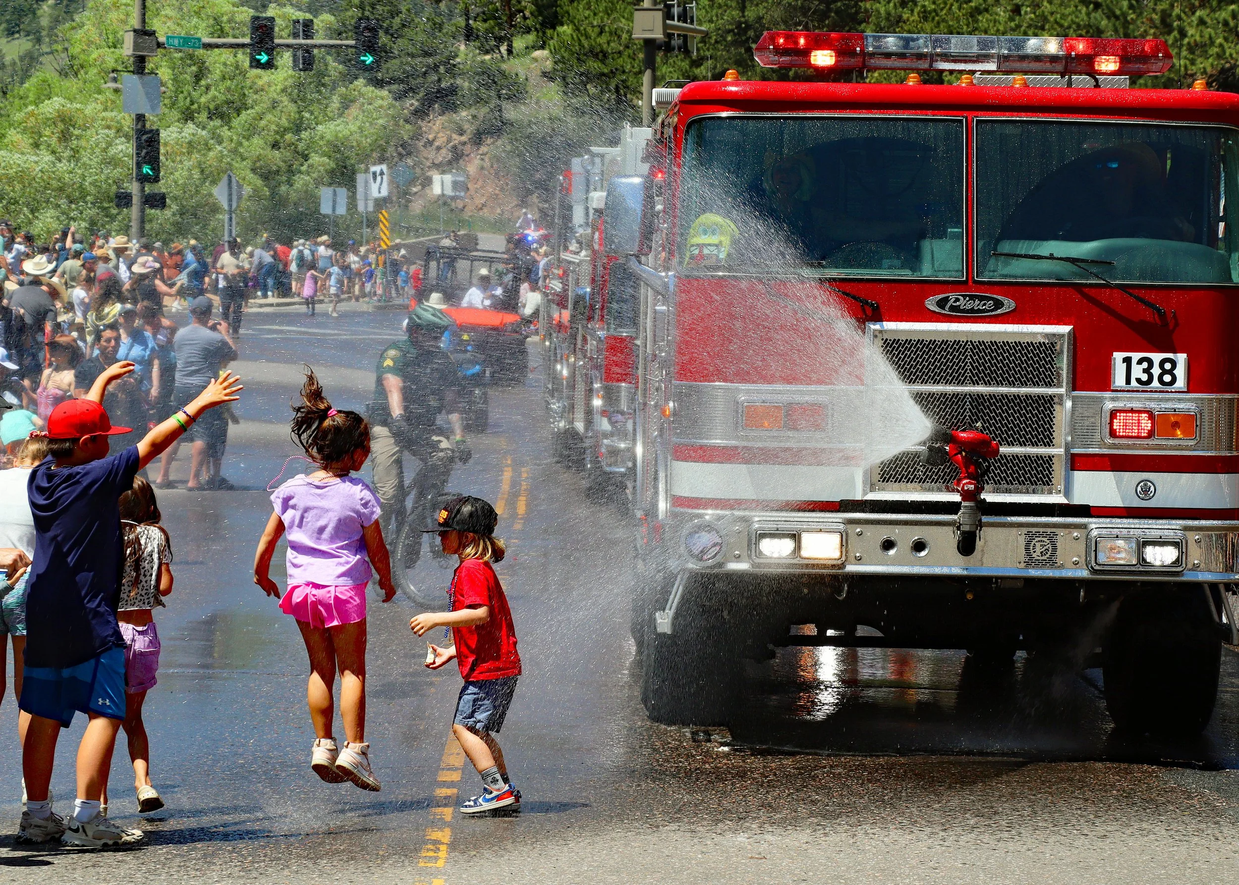 Children playing with a fire hose spraying water on the street while a red fire truck is parked nearby.