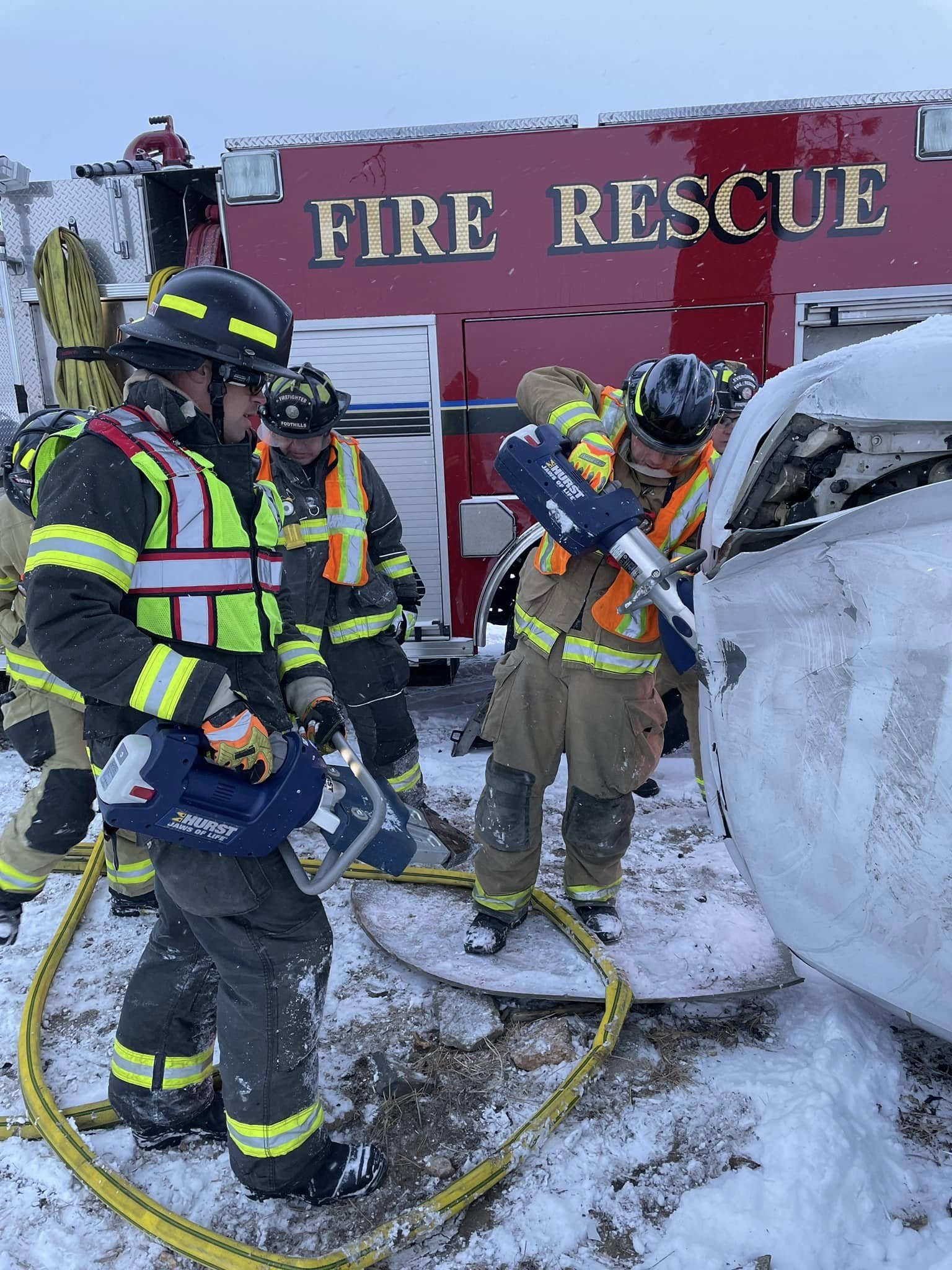 Firefighters working at the scene of a car accident in snowy conditions, with a fire rescue truck nearby.