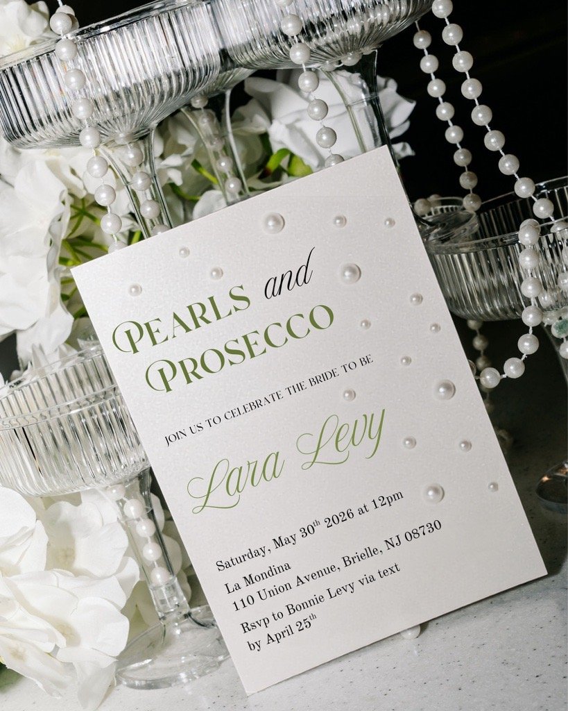 Wedding invitation for a celebration of pearls and prosecco, with white flowers, pearls, and glass candle holders.