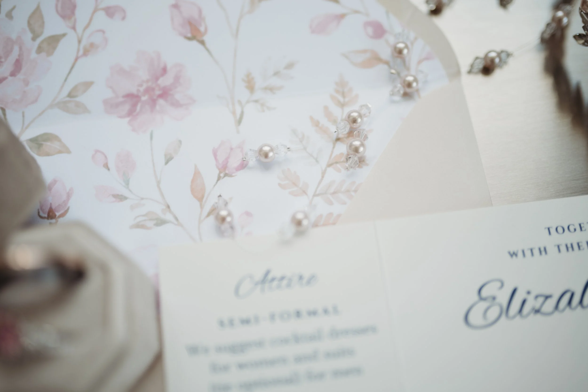 Close-up of a floral-designed card or paper with pearl and crystal bead jewelry on top, partially covering the text.