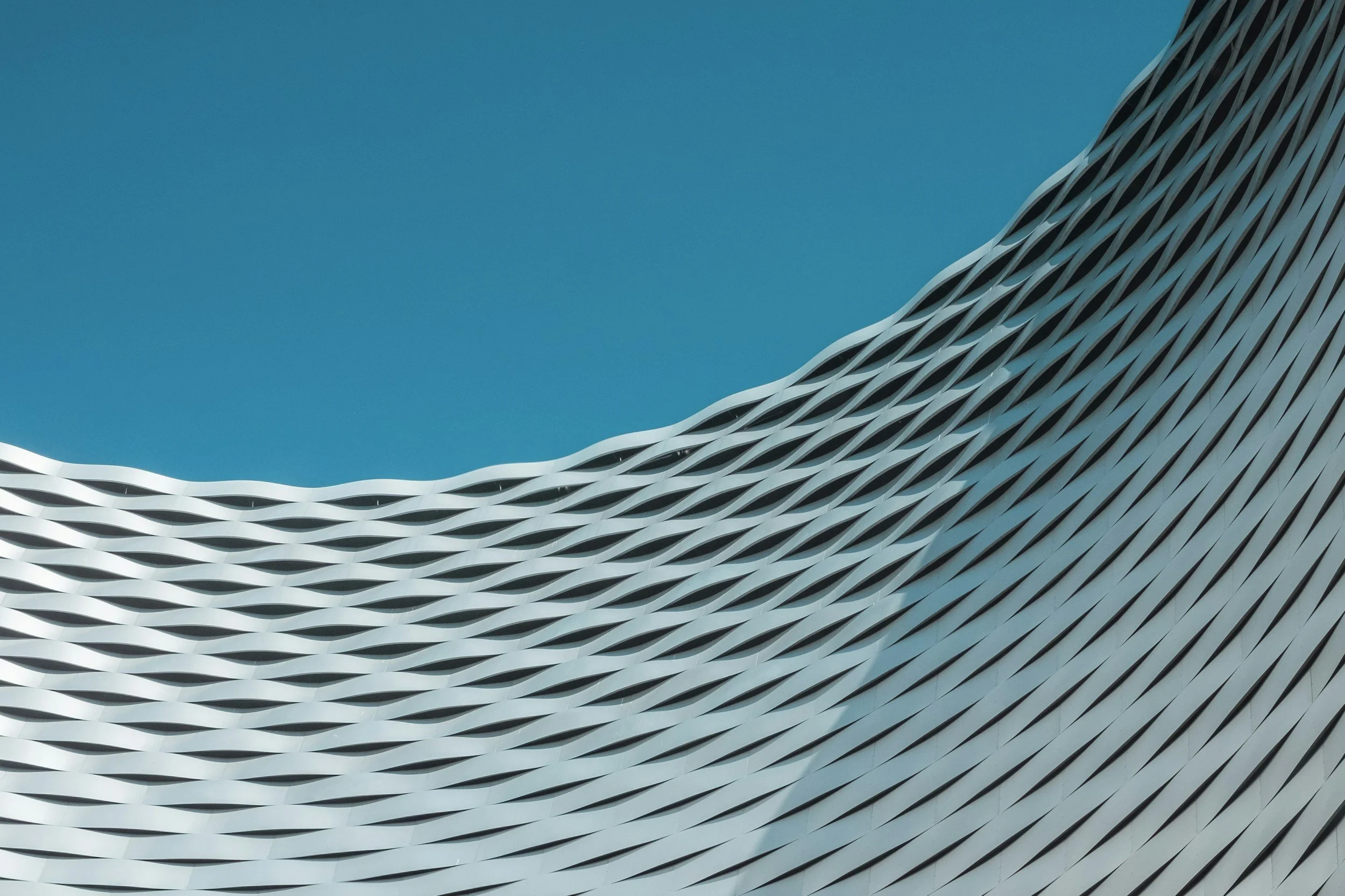 Close-up of a modern building with a textured, wave-like exterior surface against a clear blue sky.