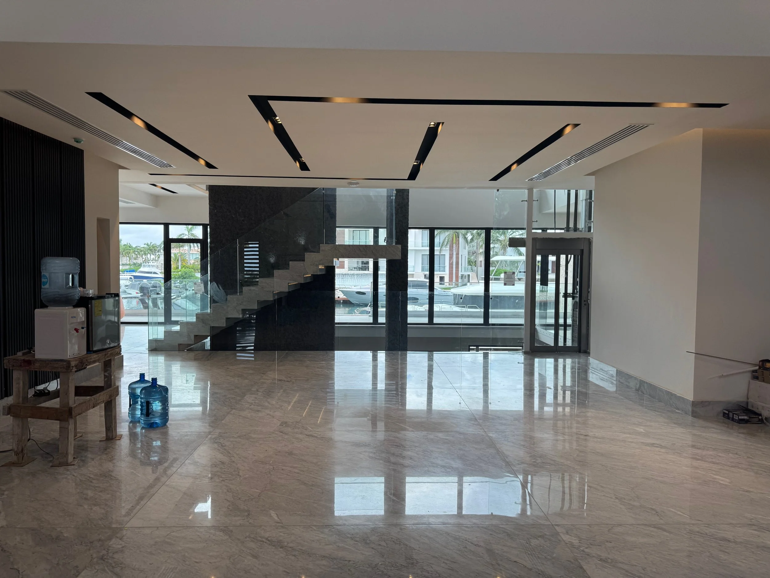 Interior of a modern building with marble floors, large glass windows, a staircase, water bottles, and a water dispenser.