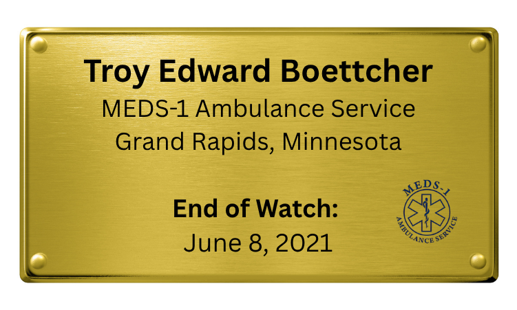 A gold-colored plaque commemorating Troy Edward Boettcher's service as an EMS paramedic in Grand Rapids, Minnesota, marking his end of watch on June 8, 2021.