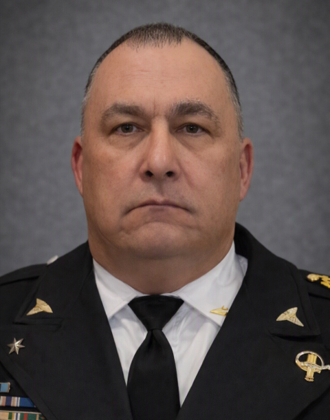 A serious-looking man in a U.S. military uniform with medals and insignia, against a neutral background.