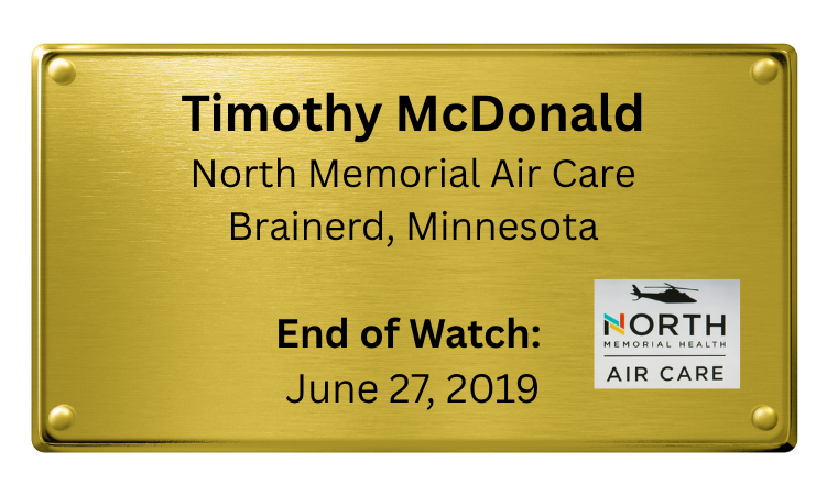 Gold-colored plaque with black text dedicated to Timothy McDonald of North Memorial Air Care, Brainerd, Minnesota, indicating the end of watch on June 27, 2019, and includes North Memorial Health Air Care logo.