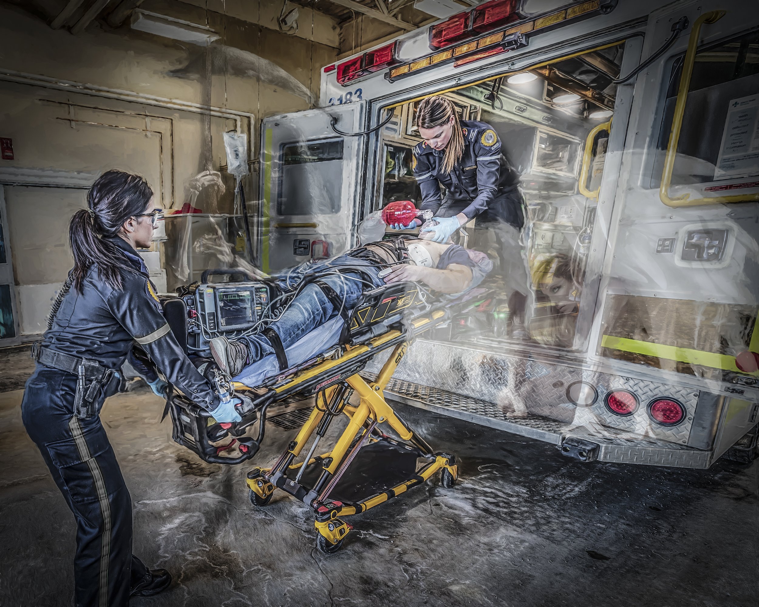 Paramedics in black uniforms are transporting a patient on a stretcher into an ambulance. The patient is connected to medical equipment, and one paramedic is adjusting the patient's airway while another oversees the process. The scene appears to be in an indoor emergency medical setting.