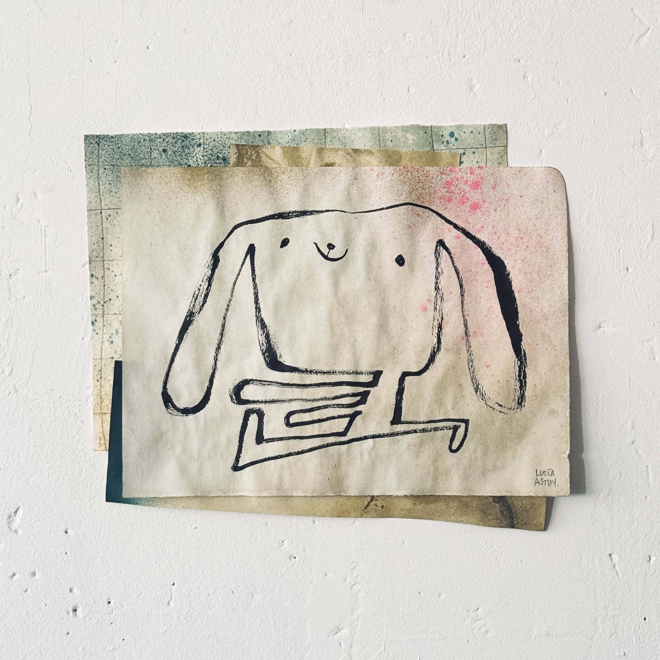 Dibujo de un perro con letras y firmas en el centro, enmarcado con cinta adhesiva en las esquinas, con fondo blanco y algunas manchas rosa y azul por Lucía Astuy.