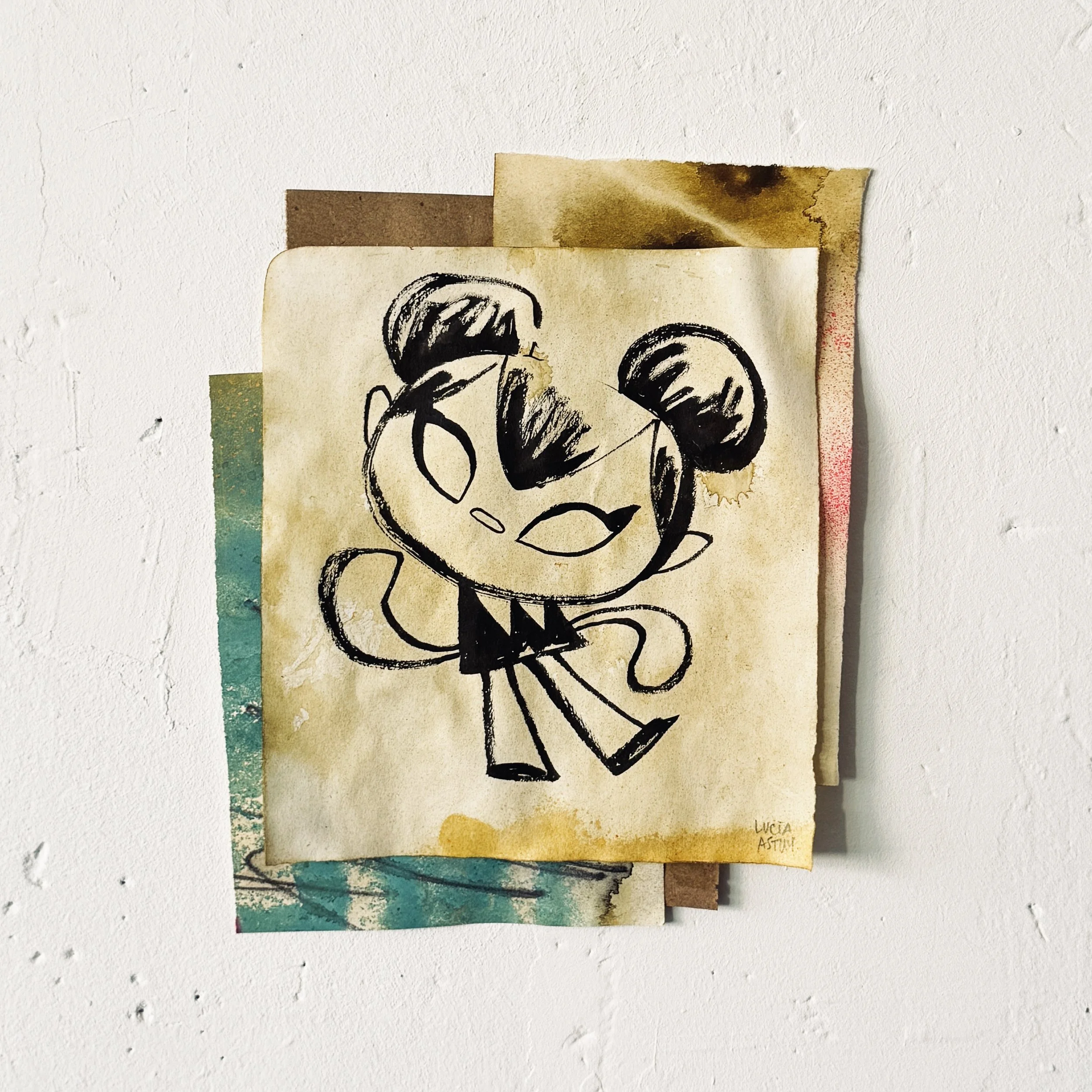 Tres papeles con dibujos y escritura en ellos, pegados en una pared blanca. Uno de los papeles tiene un dibujo de una cara con cabello y bigote, acompañado del texto 'LUCÍA ASTUY'.