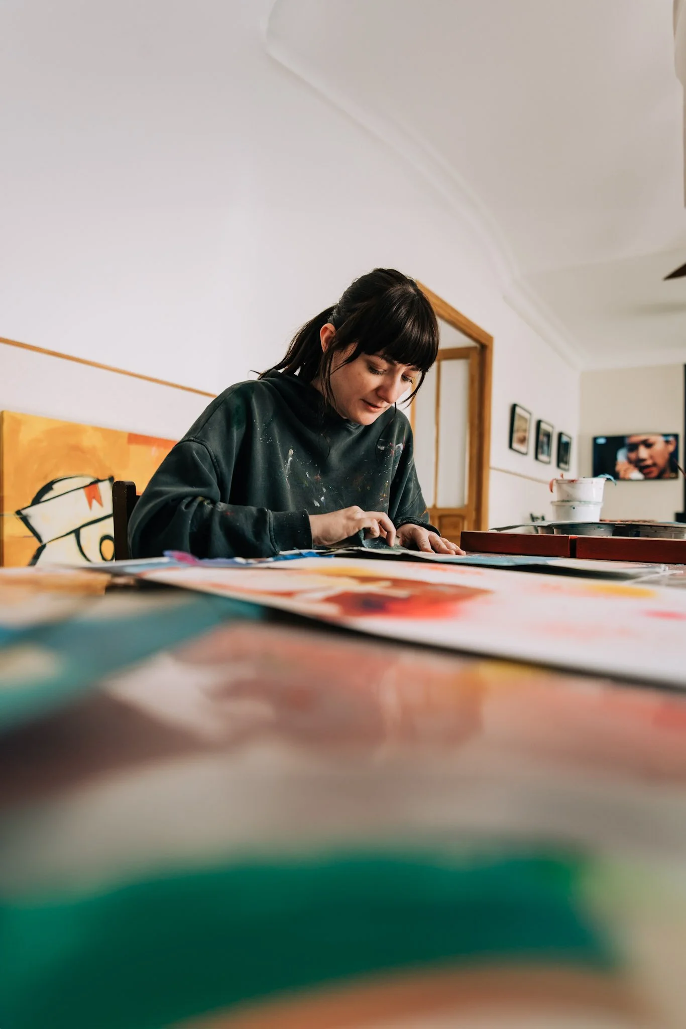 Joven mujer pintando en un taller de arte, rodeada de pinturas y materiales de pintura.