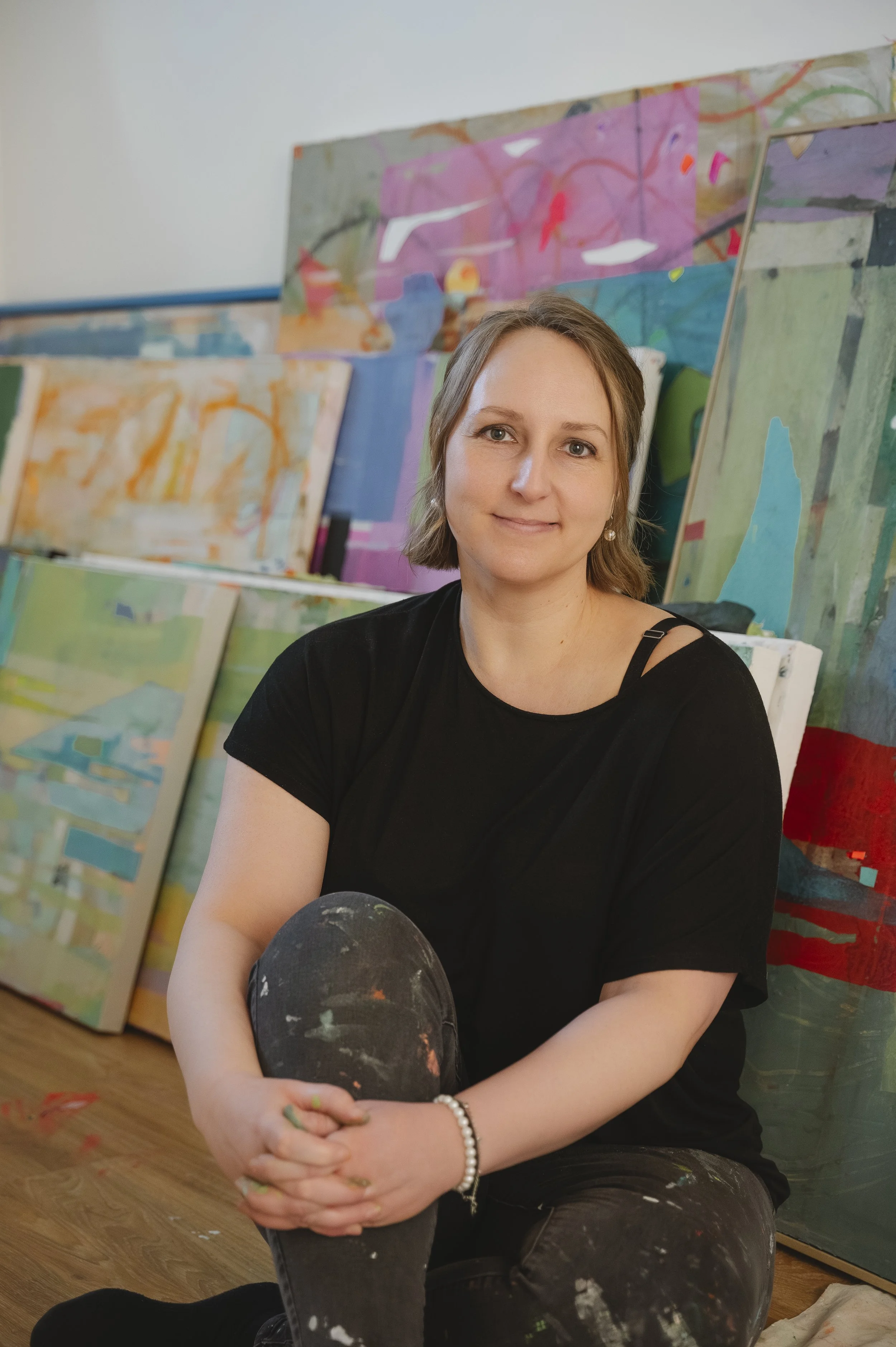 A woman sitting in front of several colorful abstract paintings.