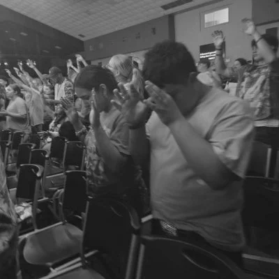People standing and praying in a church or worship setting with raised hands.