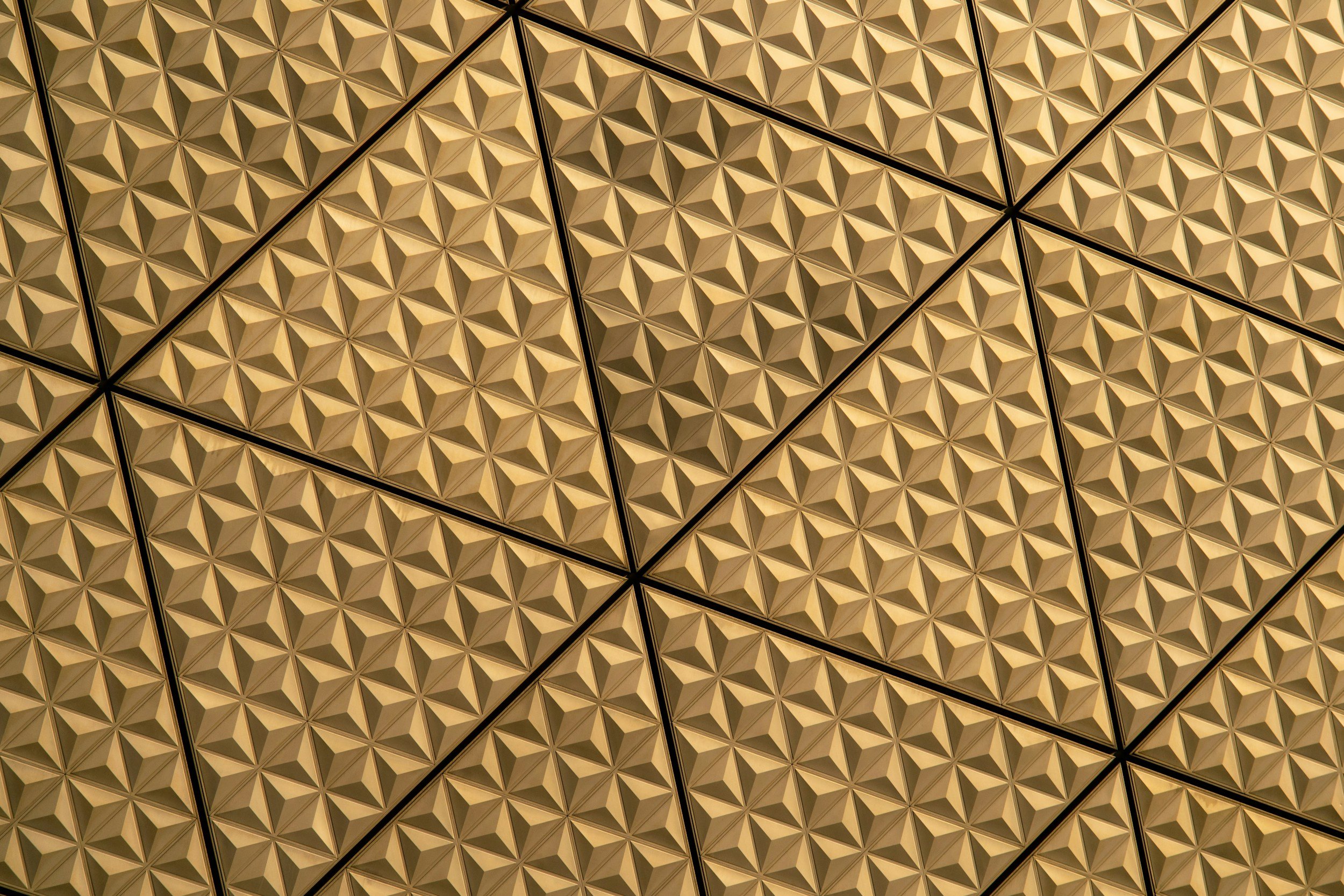 Close-up of golden, geometric, pyramid-shaped ceiling tiles arranged in a pattern.