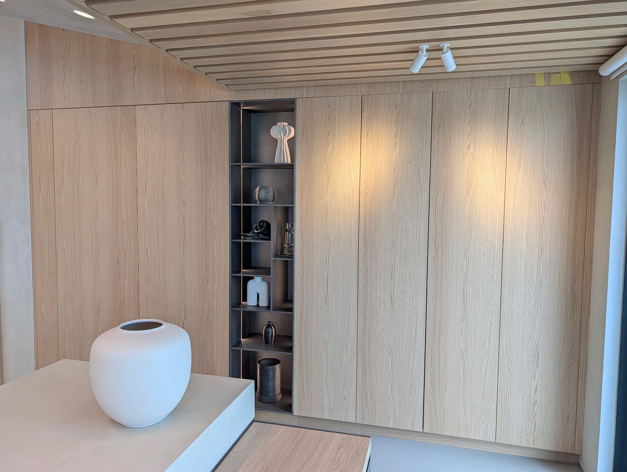 Modern interior space with wood-paneled wall, a built-in shelf with decorative items, and a white sphere-shaped object on a white surface.