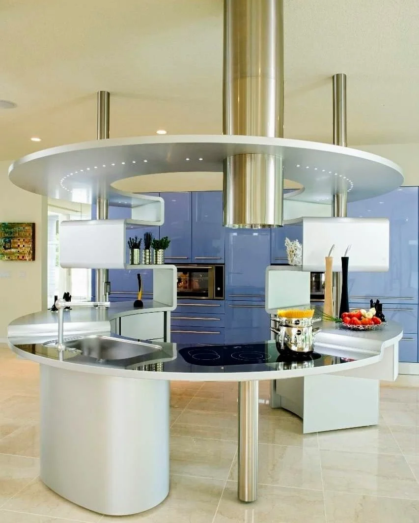 Modern kitchen with a circular white kitchen island, built-in stovetop, pot, and decorative items including fruit and candles.