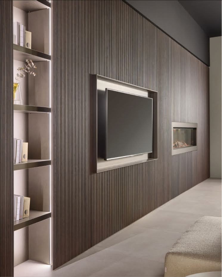 Modern living room wall with a built-in flat-screen TV and a fireplace, featuring dark wood paneling and a tall bookshelf on the left.