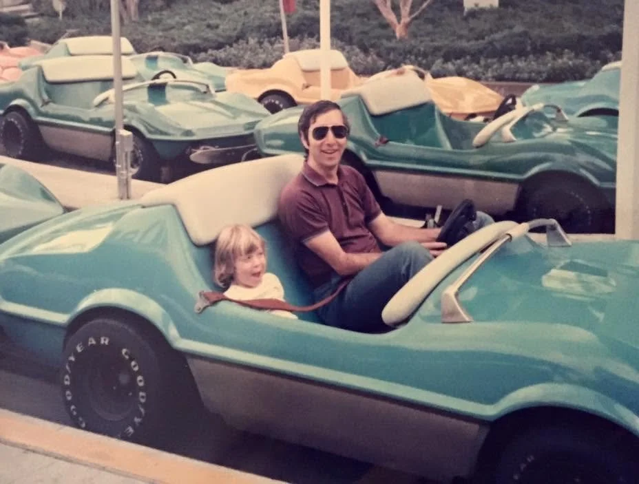 Young Lindsey Caplan at in an open top car ride with her father at Disneyland.