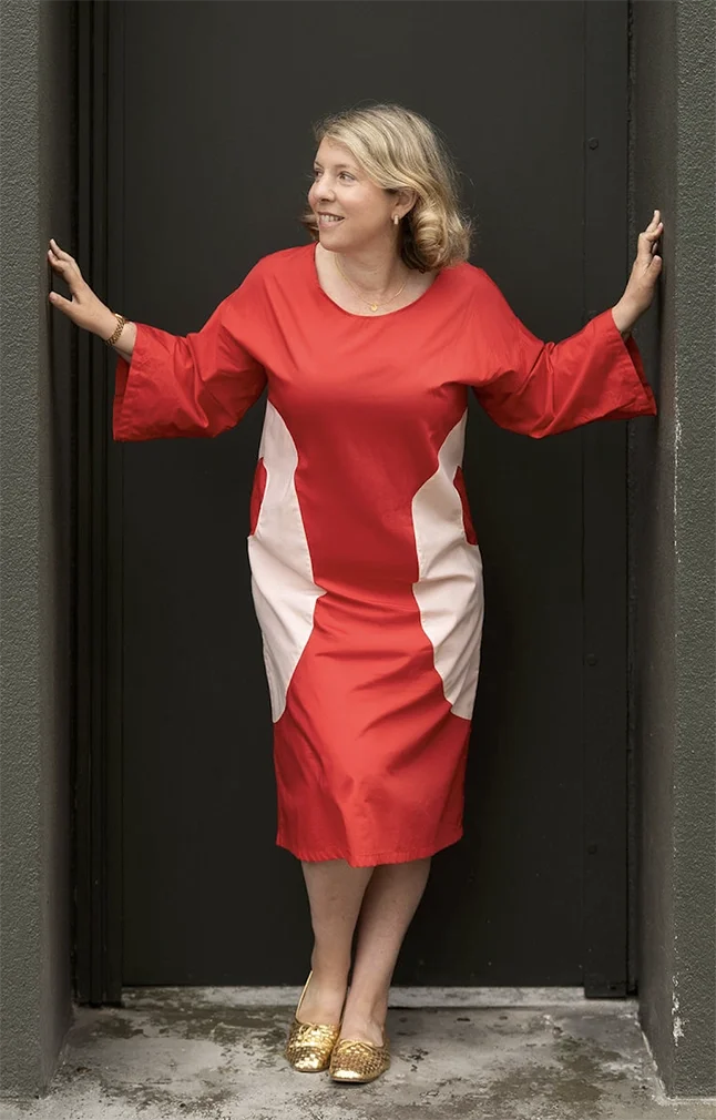 Woman in red and white dress standing in doorway with arms outstretched, smiling.