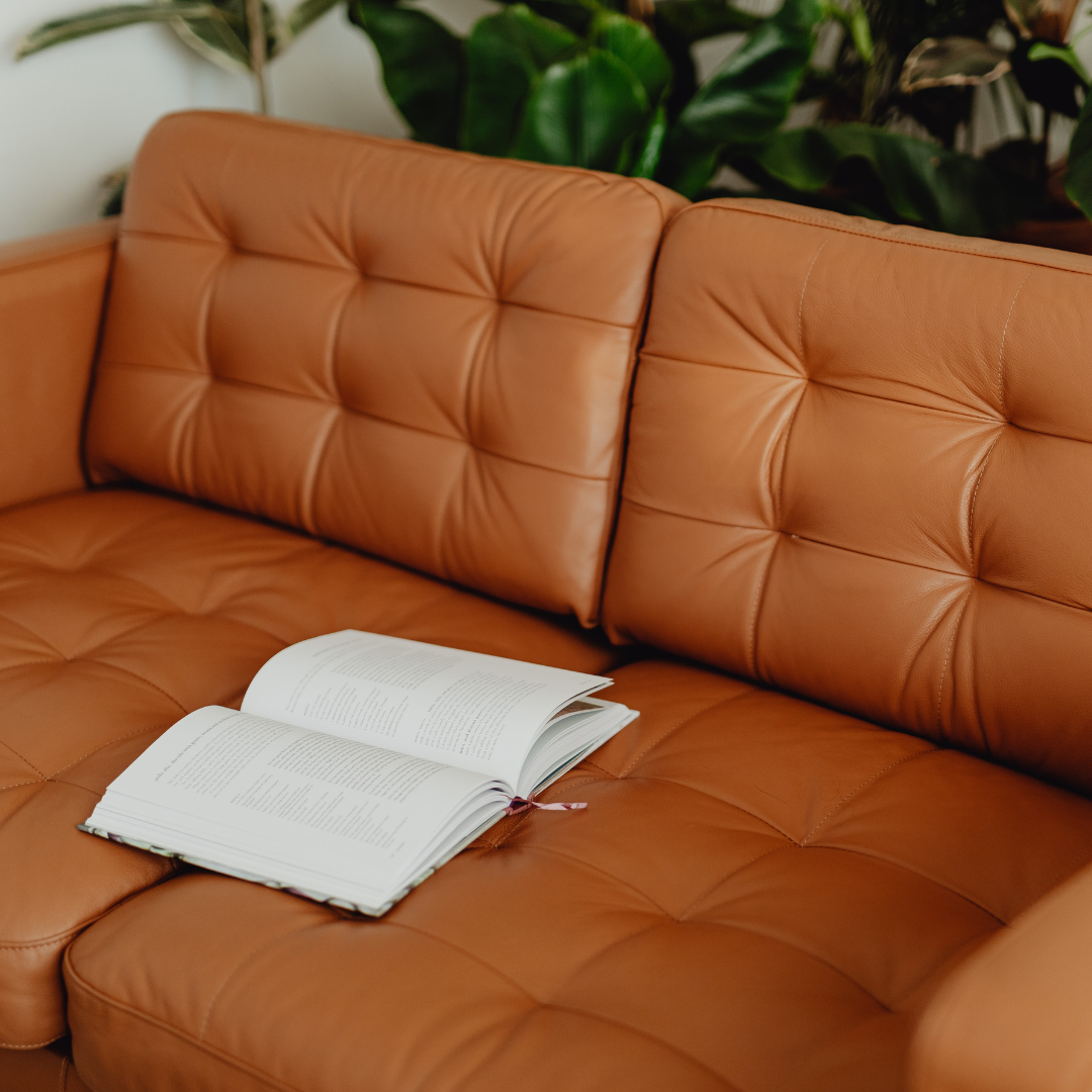 Orange leather tufted sofa with an open book resting on it, and green plants in the background.