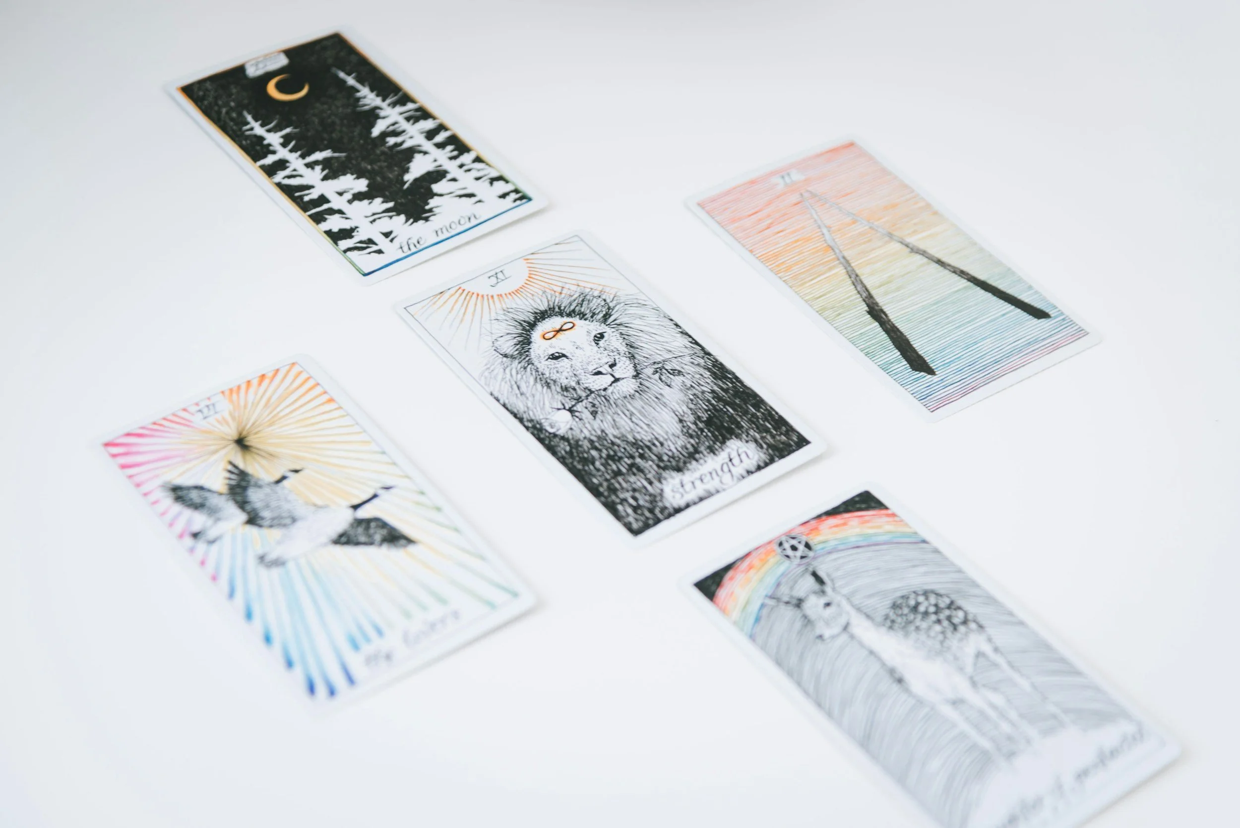 A spread of five tarot cards on a white surface, including The Moon, Strength, and two others with colorful, intricate designs.