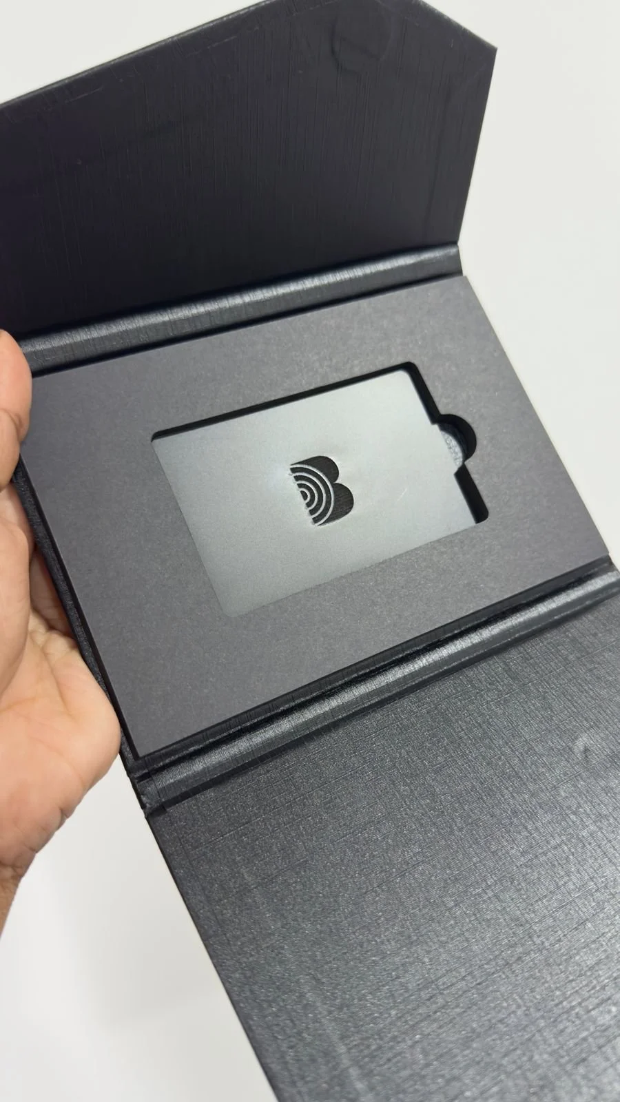 Open black box revealing a card with a black logo, inside a foam cutout.