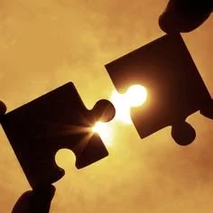 Two hands holding interconnected puzzle pieces against a sunset background.