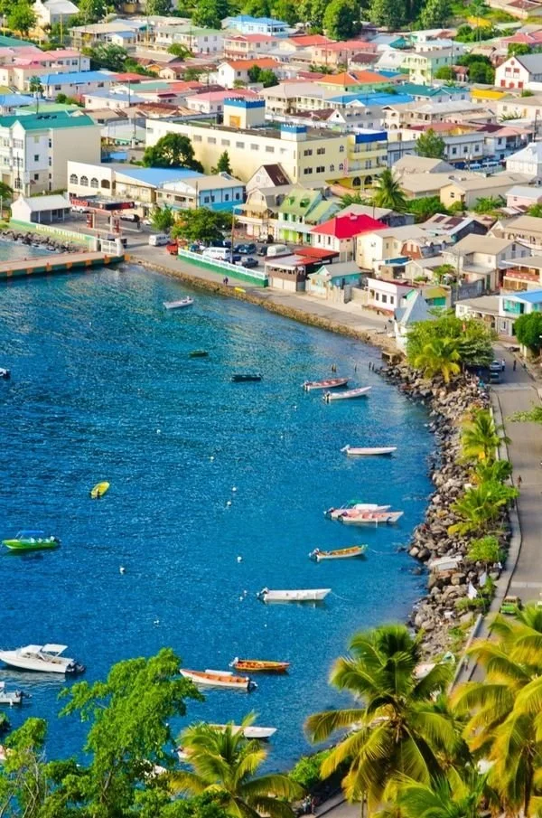 Aerial view of a coastal town Ans La Raye, St Lucia with colorful buildings, boats docked along the shoreline, and lush palm trees.