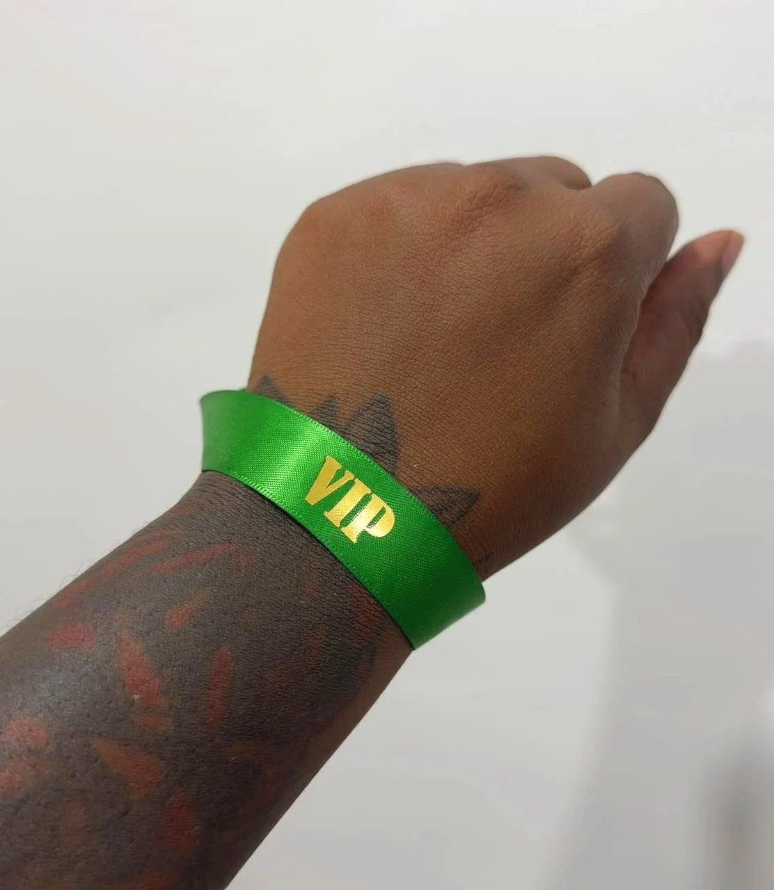 A person's hand and wrist with a green VIP wristband and colorful tattoos, against a white background.