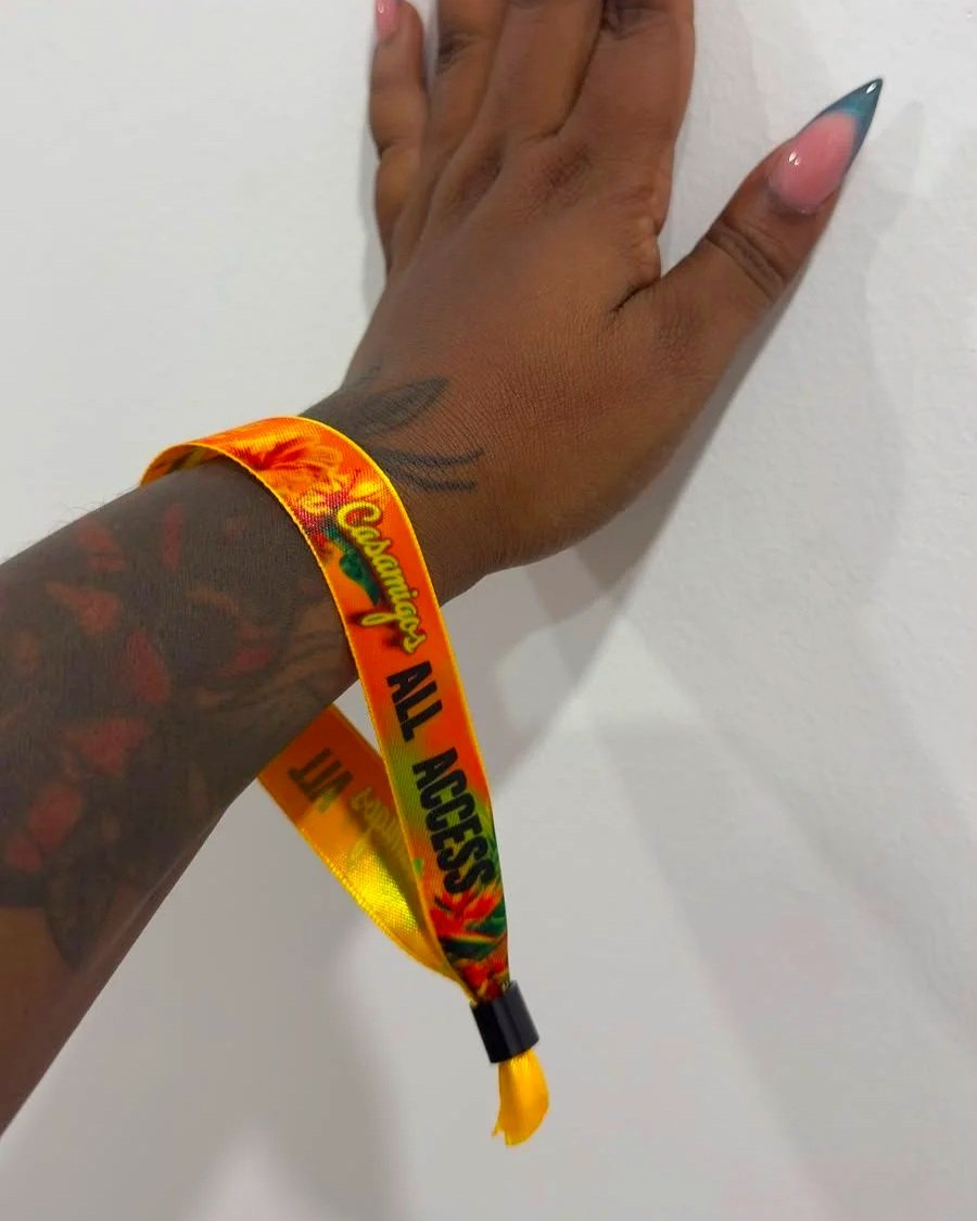 Person's hand with colorful tattoos wearing a yellow, red, and green 'All Access' wristbands against a white wall.