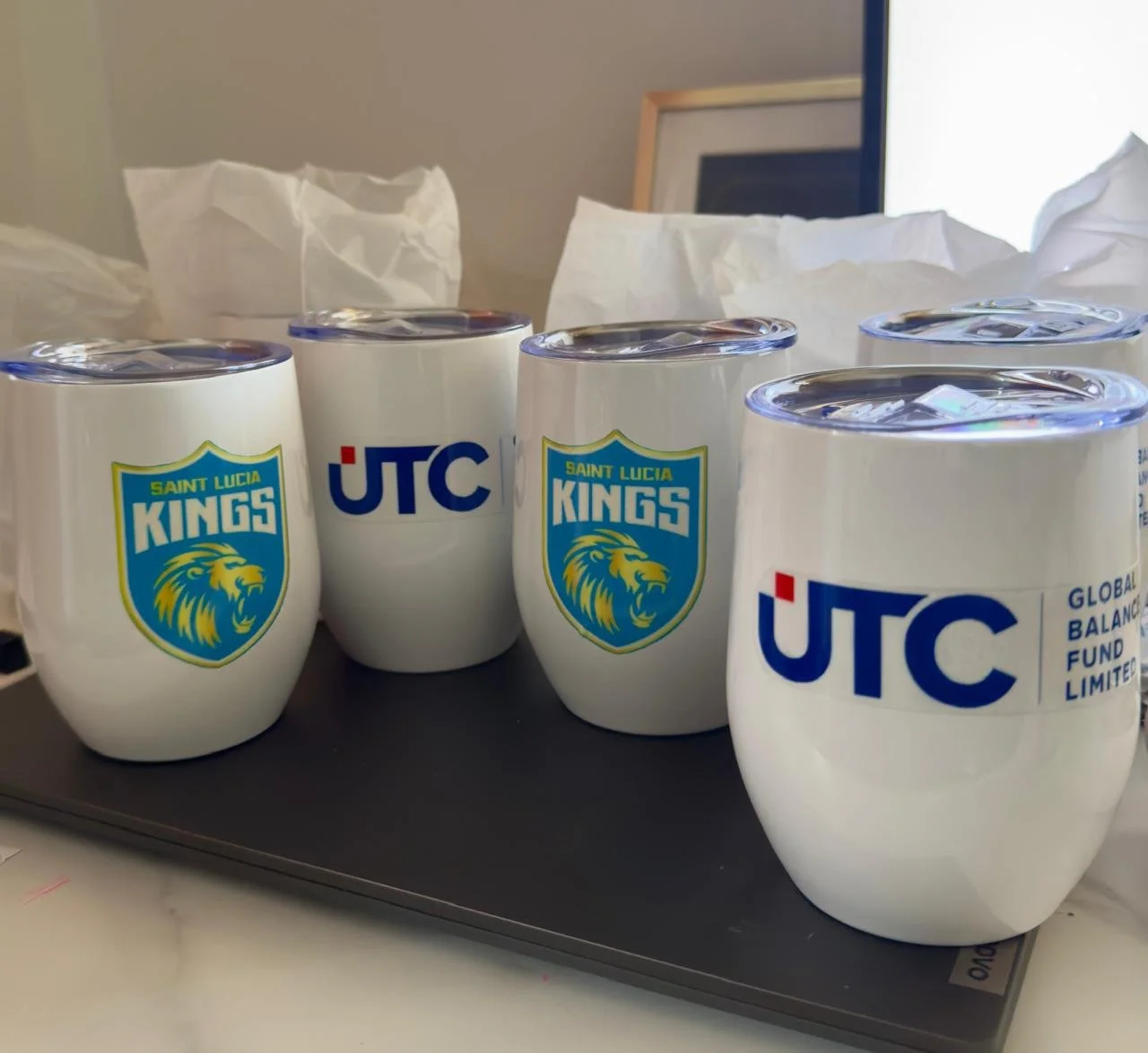 White mugs with the logos of Saint Lucia Kings and UTC on a table.