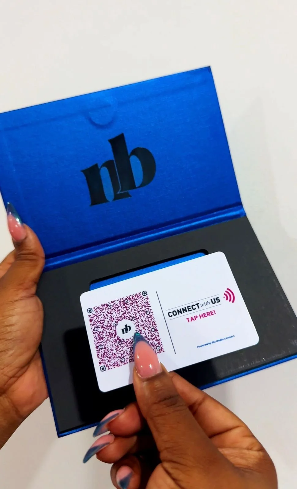 Person using their finger to scan a QR code on a card that says 'Connect with Us, Tap Here' inside a blue box with 'nb' logo on the top.