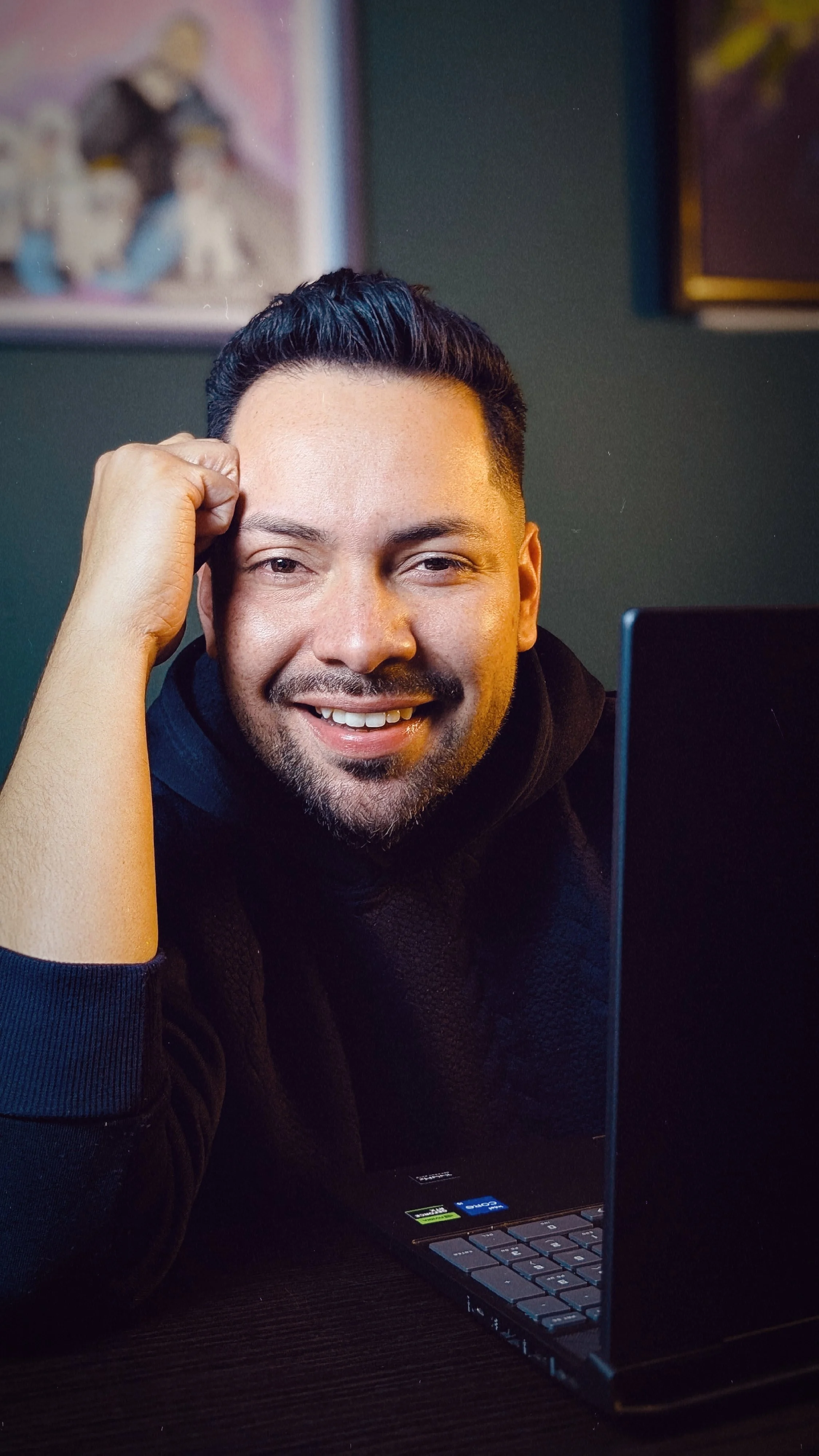 Hombre sonriendo y descansando la cabeza en su mano frente a una laptop en un ambiente interior.