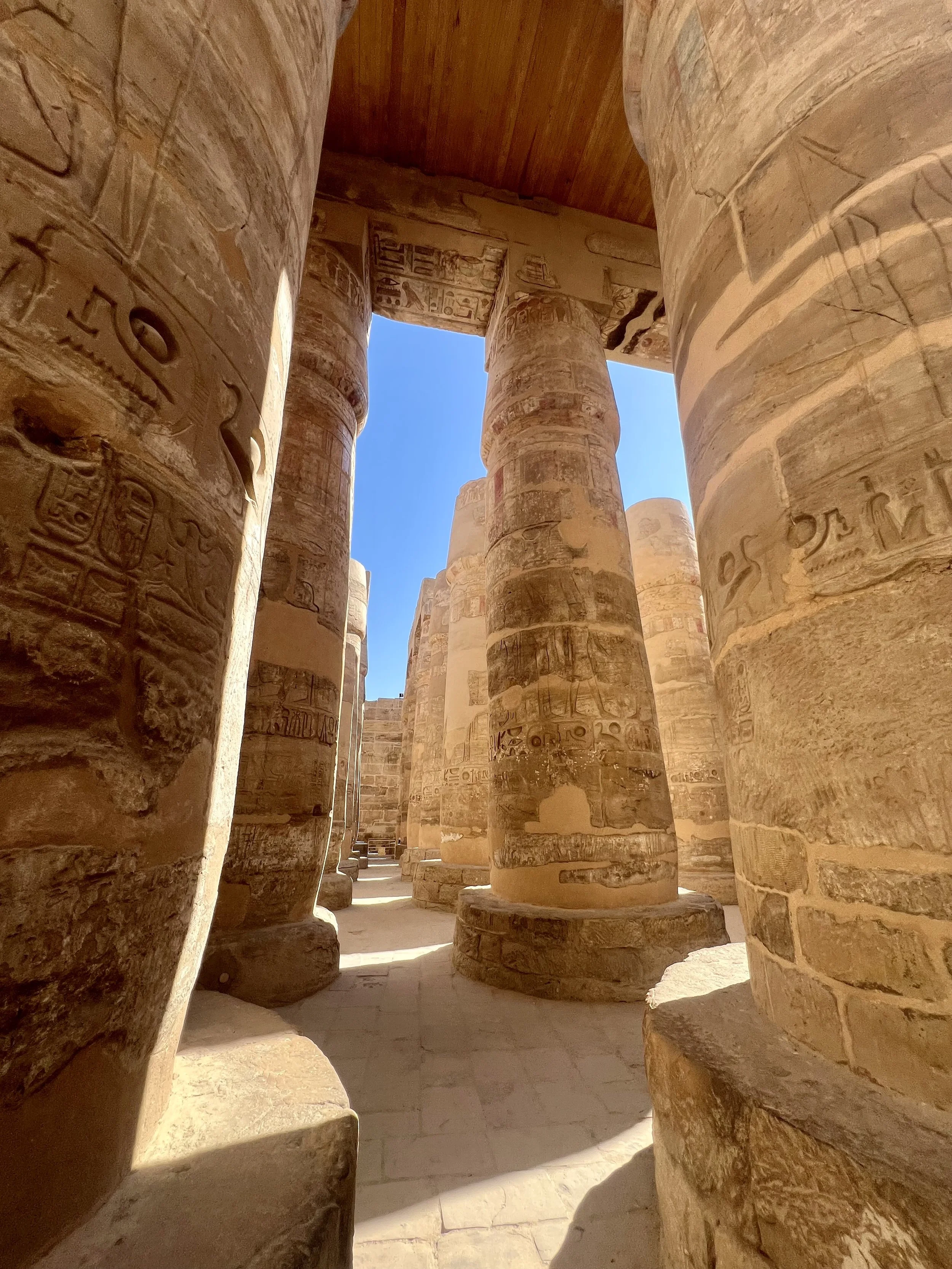 Interior view of ancient Egyptian temple with large stone columns decorated with hieroglyphics, sunlight casting shadows on the floor.