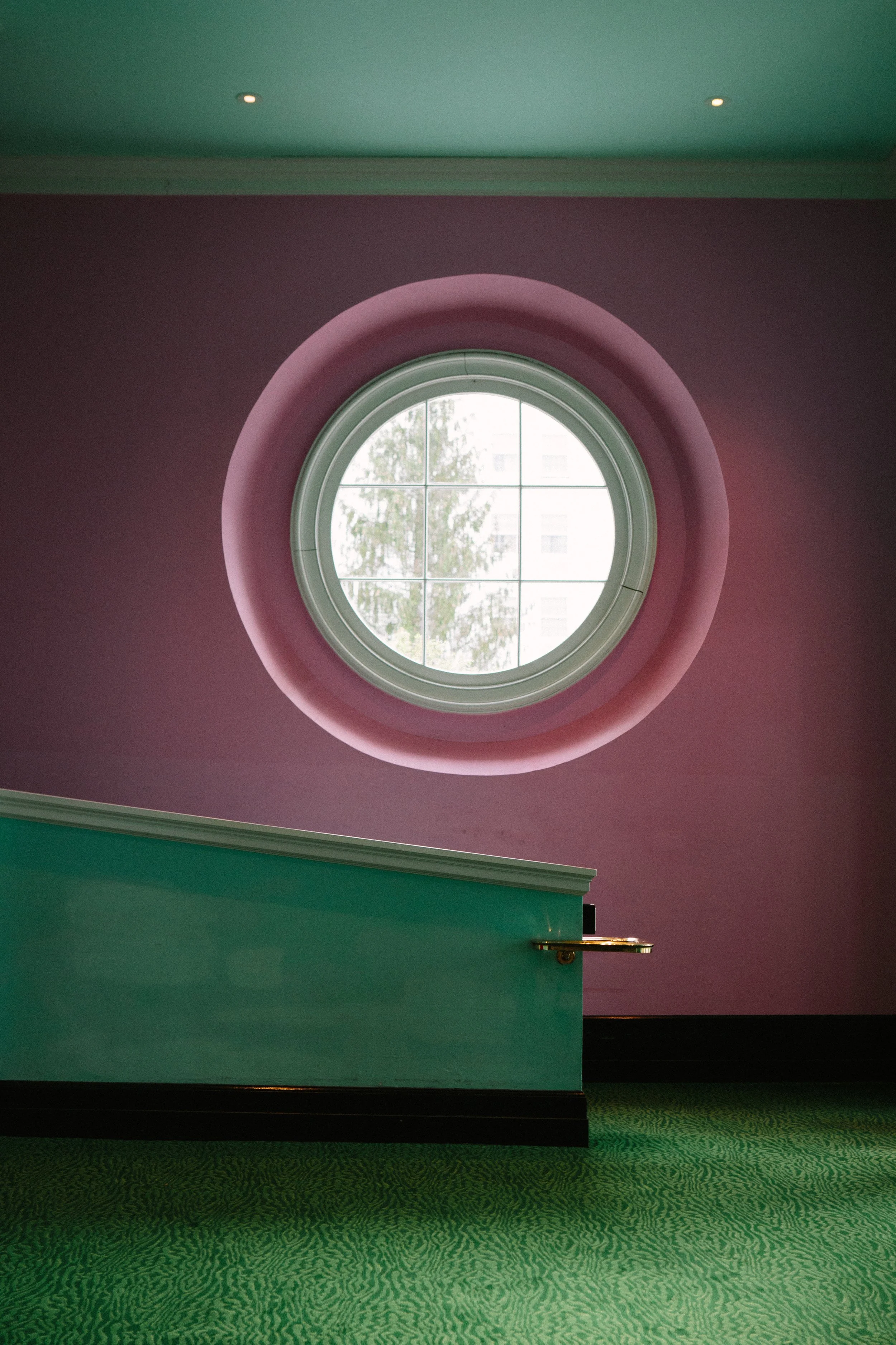 Interior with a round window on a purple wall, green ceiling, teal window casing, and green carpeted floor.