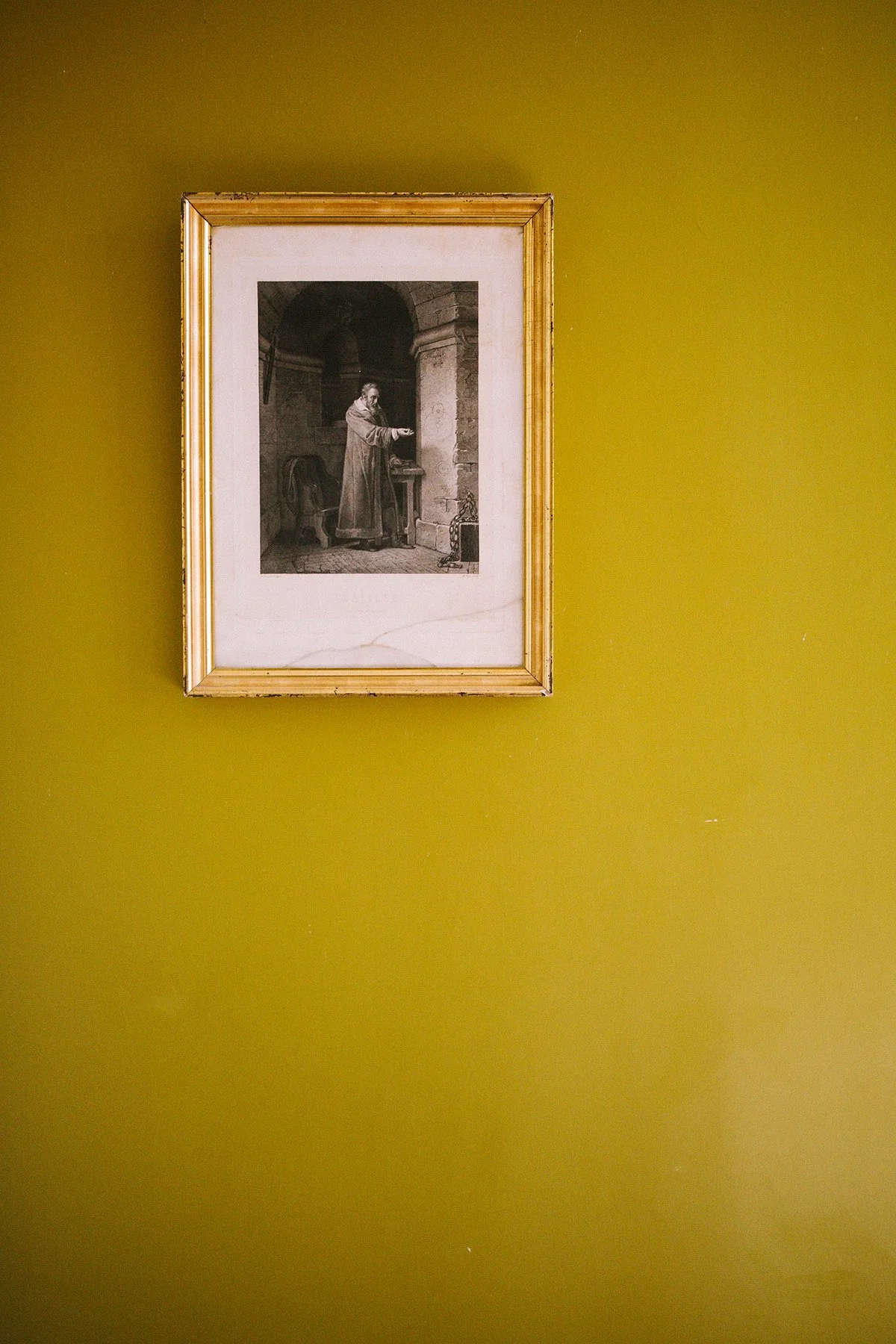 interior image of an ochre-colored wall with a black and white framed drawing of a man in historical costume standing in a stone room with an arched ceiling, pointing or reaching out - Chateau St. Julien, Poitiers, France.