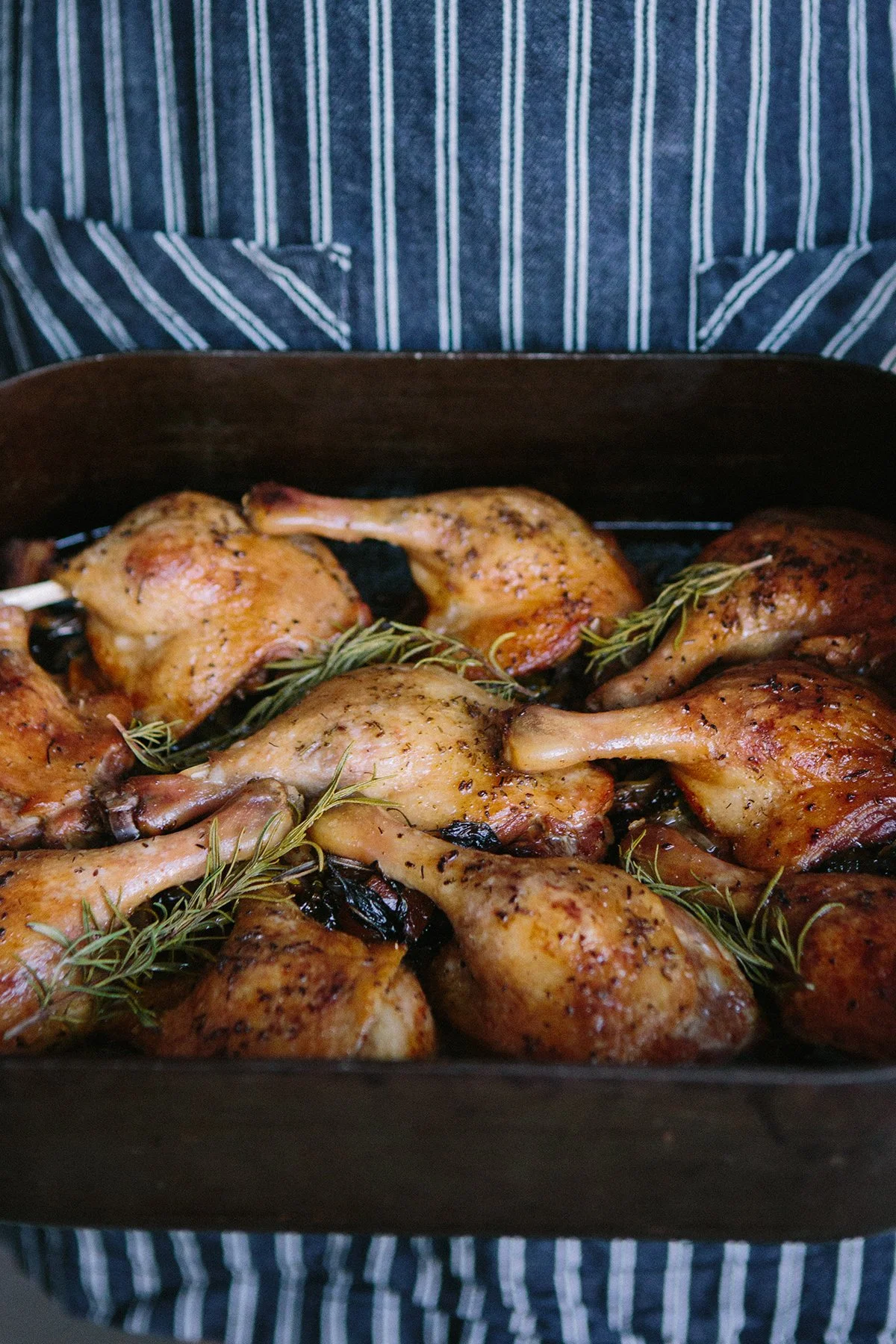 Roasted duck legs / thighs garnished with rosemary in a black cast-iron baking dish.