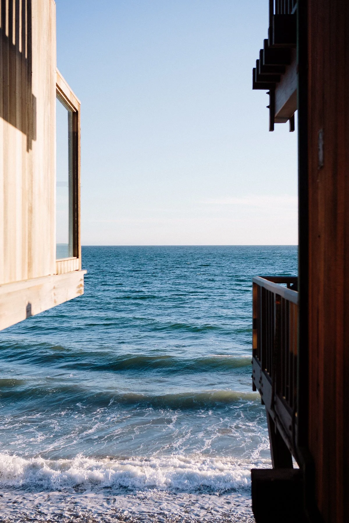 View of the ocean between two wooden beachfront homes on either side, in Malibu.