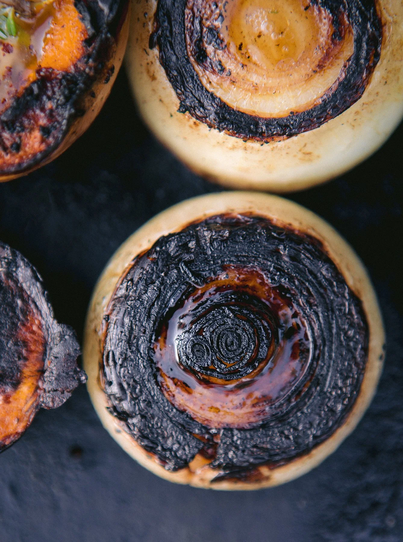 Close-up of caramelized / grilled onion slices with charred edges, placed on a dark surface.