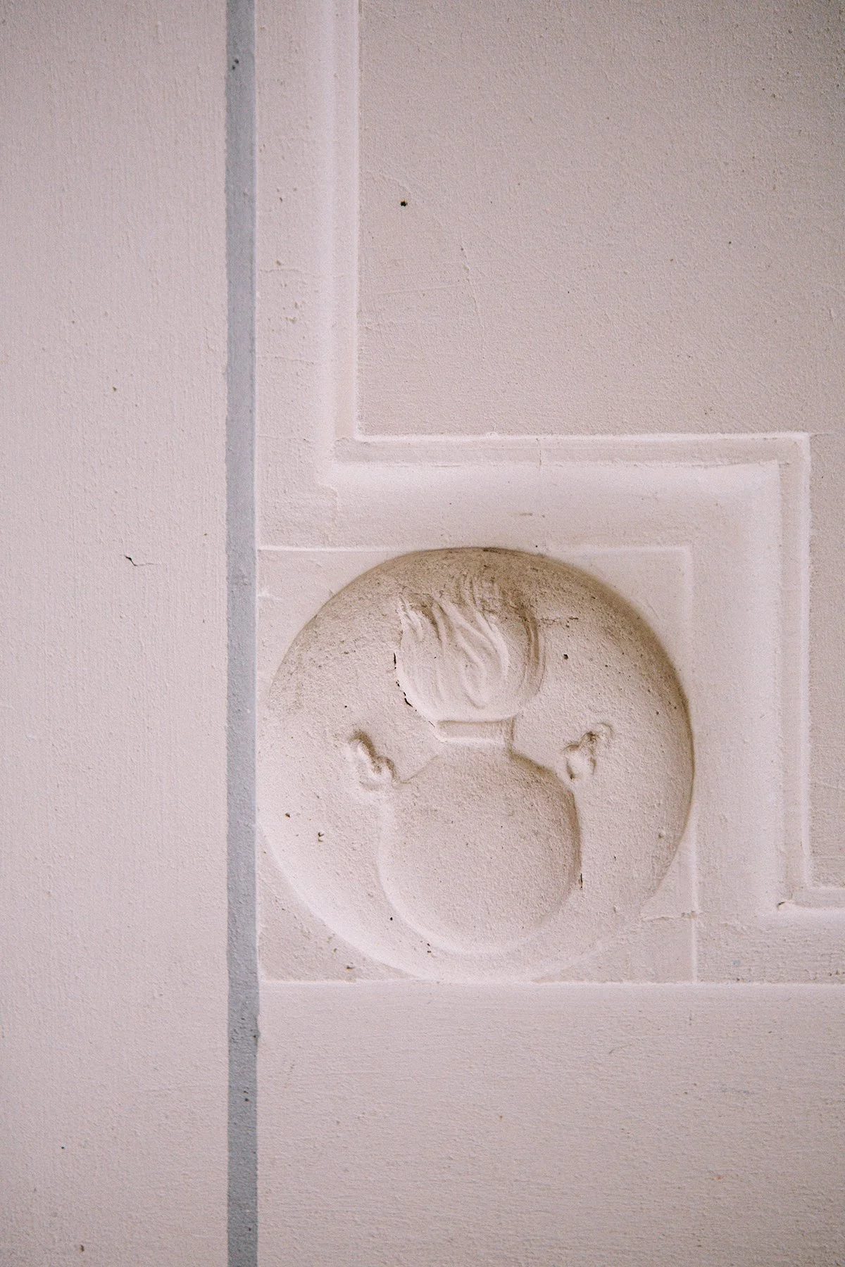 Architectural detail of a white wall with a circular decorative detail featuring a carved design, of a flaming cauldron in the kitchen of Chateau St. Julien, Poitiers, France.