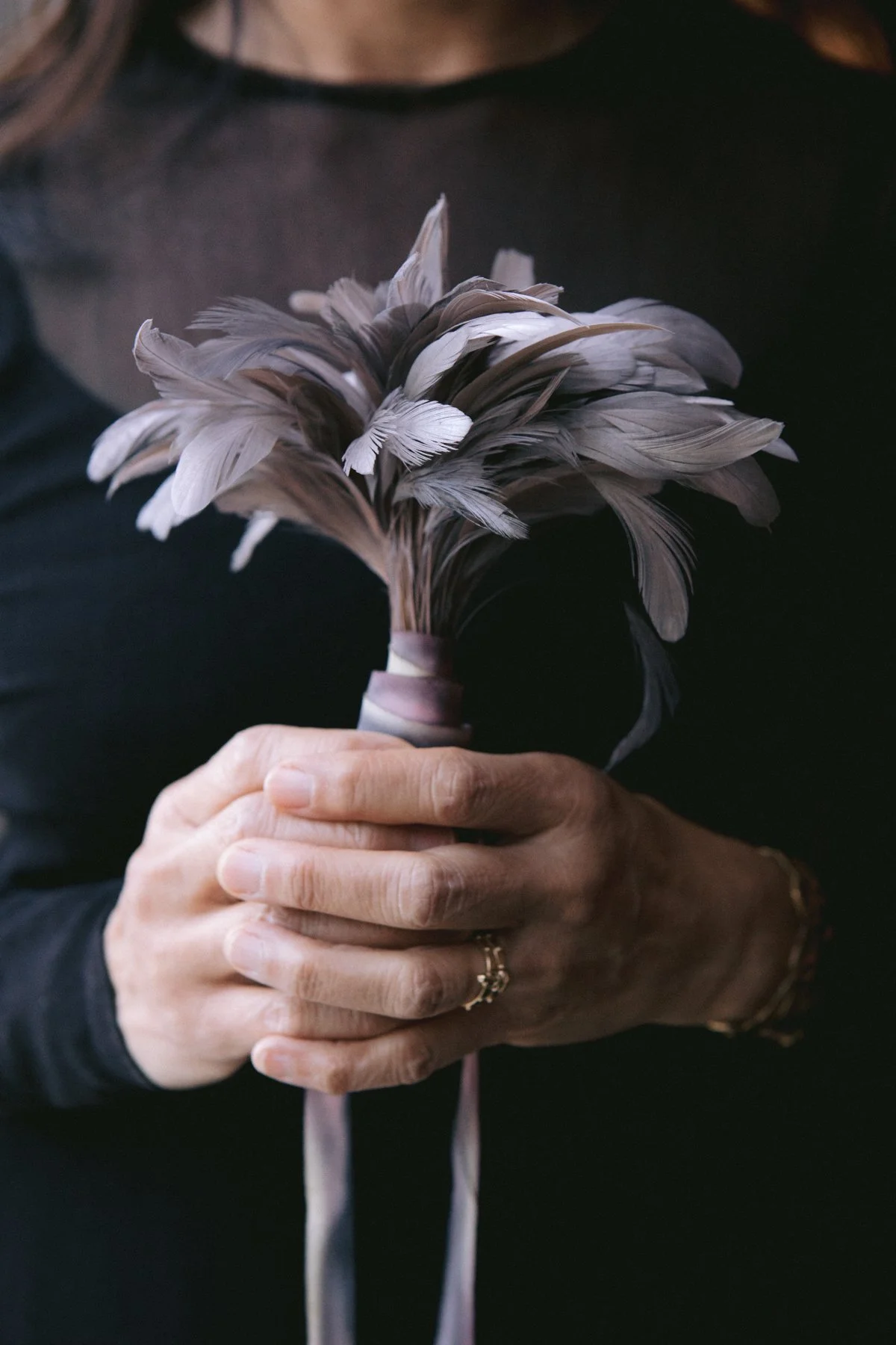 A person holding a bouquet of gray and brown feathers with both hands.