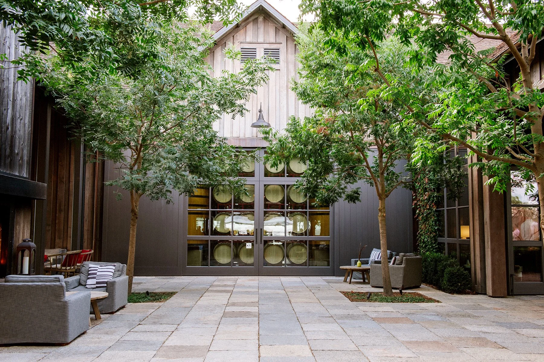 Exterior architectural photograph of Ram's Gate Winery in Sonoma, California, featuring a wood-clad gabled structure, large glass doors displaying wine barrels, and a landscaped patio.