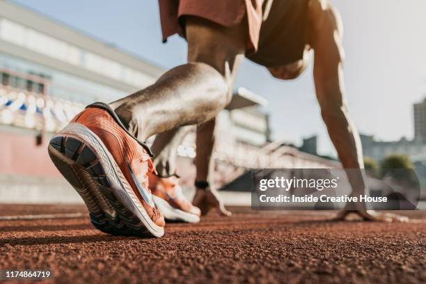 Close-up of a person's feet in running shoes in an athletic starting position on a running track, with a cityscape background.