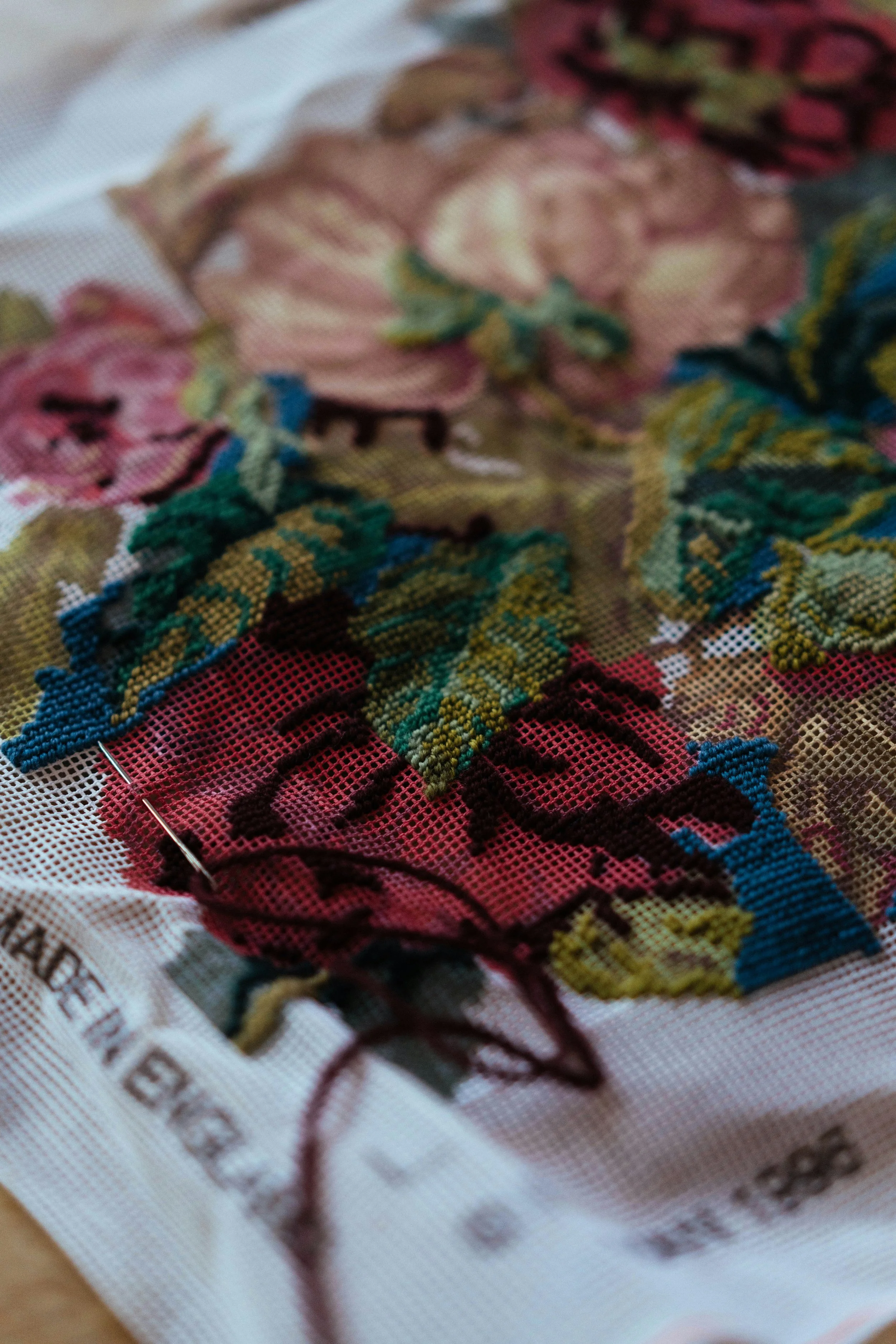 Close-up of a cross-stitch embroidery piece featuring colorful floral and geometric patterns on a white fabric background.